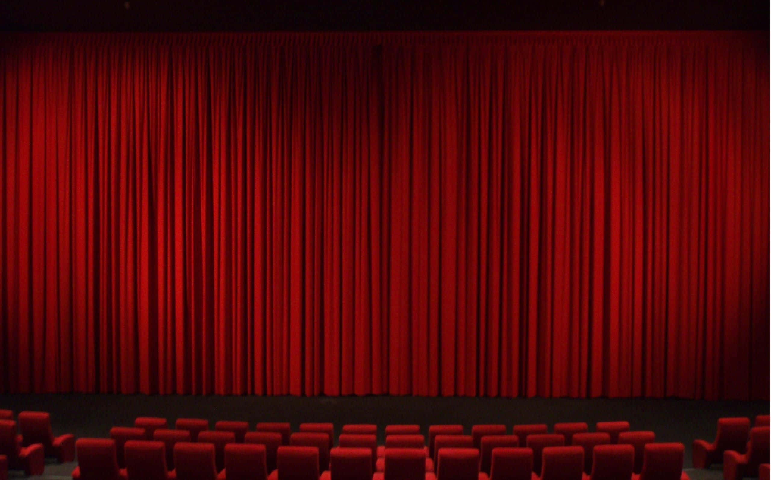Theater 桌布 壁紙 — 一排排紅色劇院座位面向一個宏大的閉合紅色天鵝絨窗簾，在燈光昏暗的禮堂中。