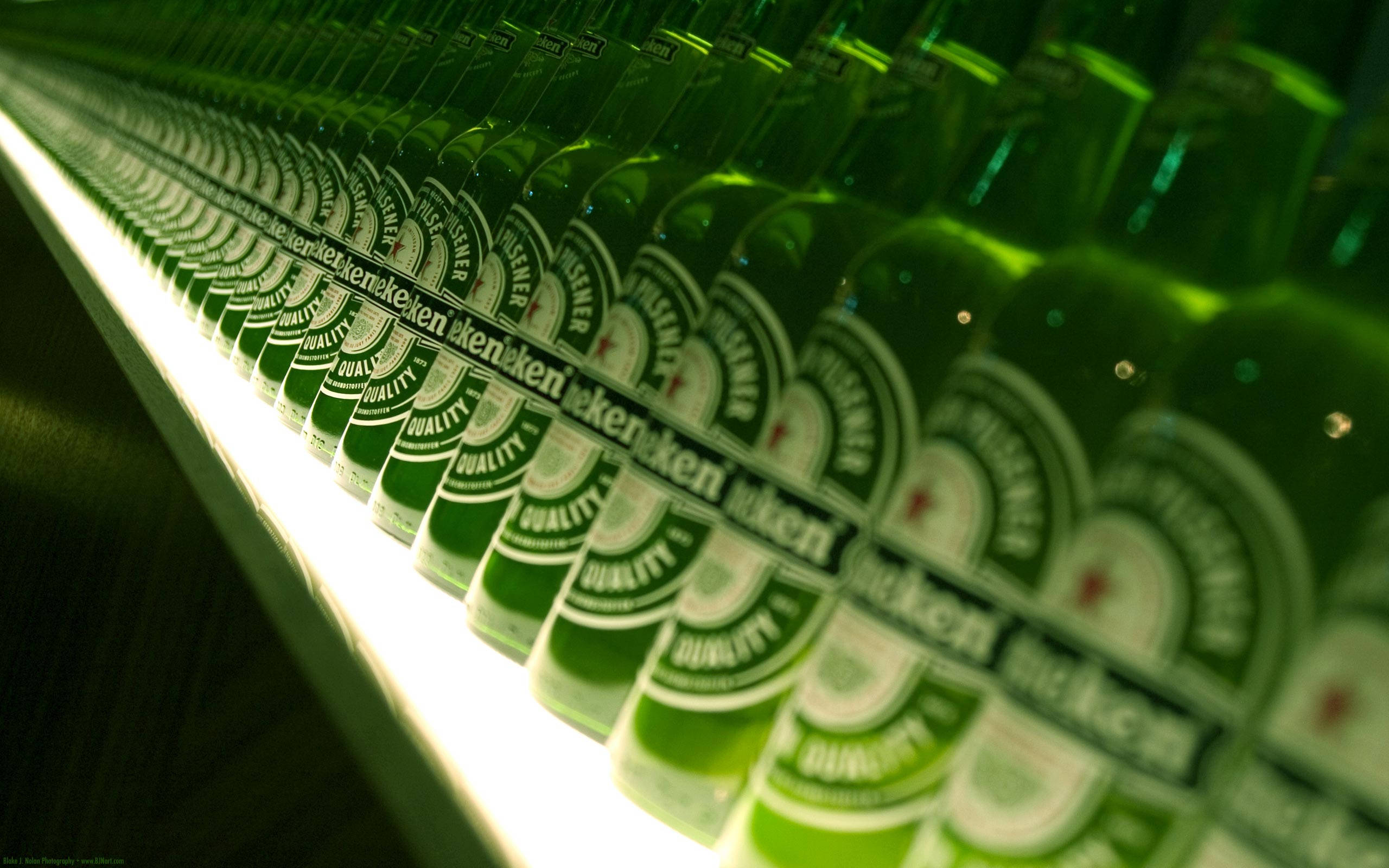 Drink 桌布 壁紙 — 一排排綠色海尼根啤酒瓶在明亮的螢光燈下於冷藏展示櫃中閃閃發光。