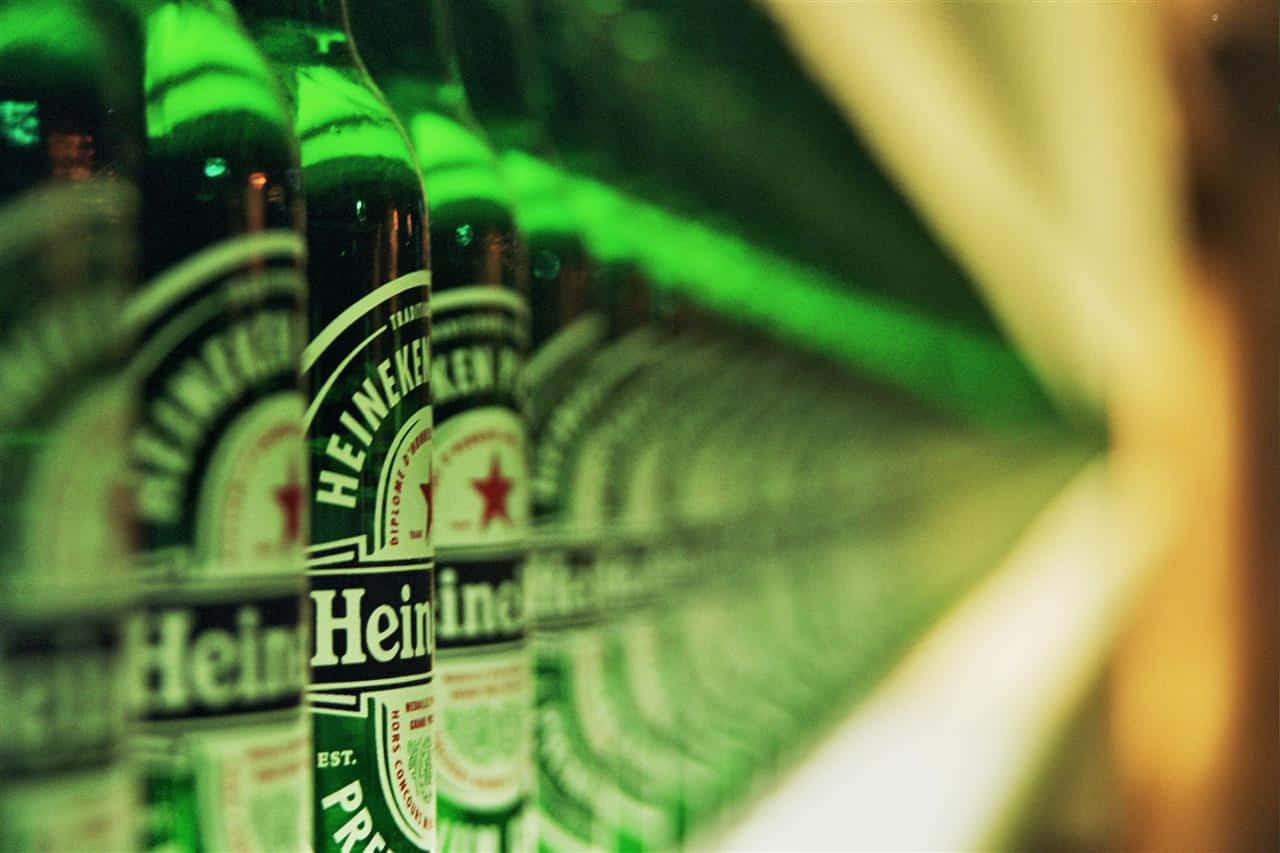 Heineken 桌布 壁紙 — 一排排綠色海尼根啤酒瓶在溫暖燈光下閃爍，淺景深凸顯前景標籤。