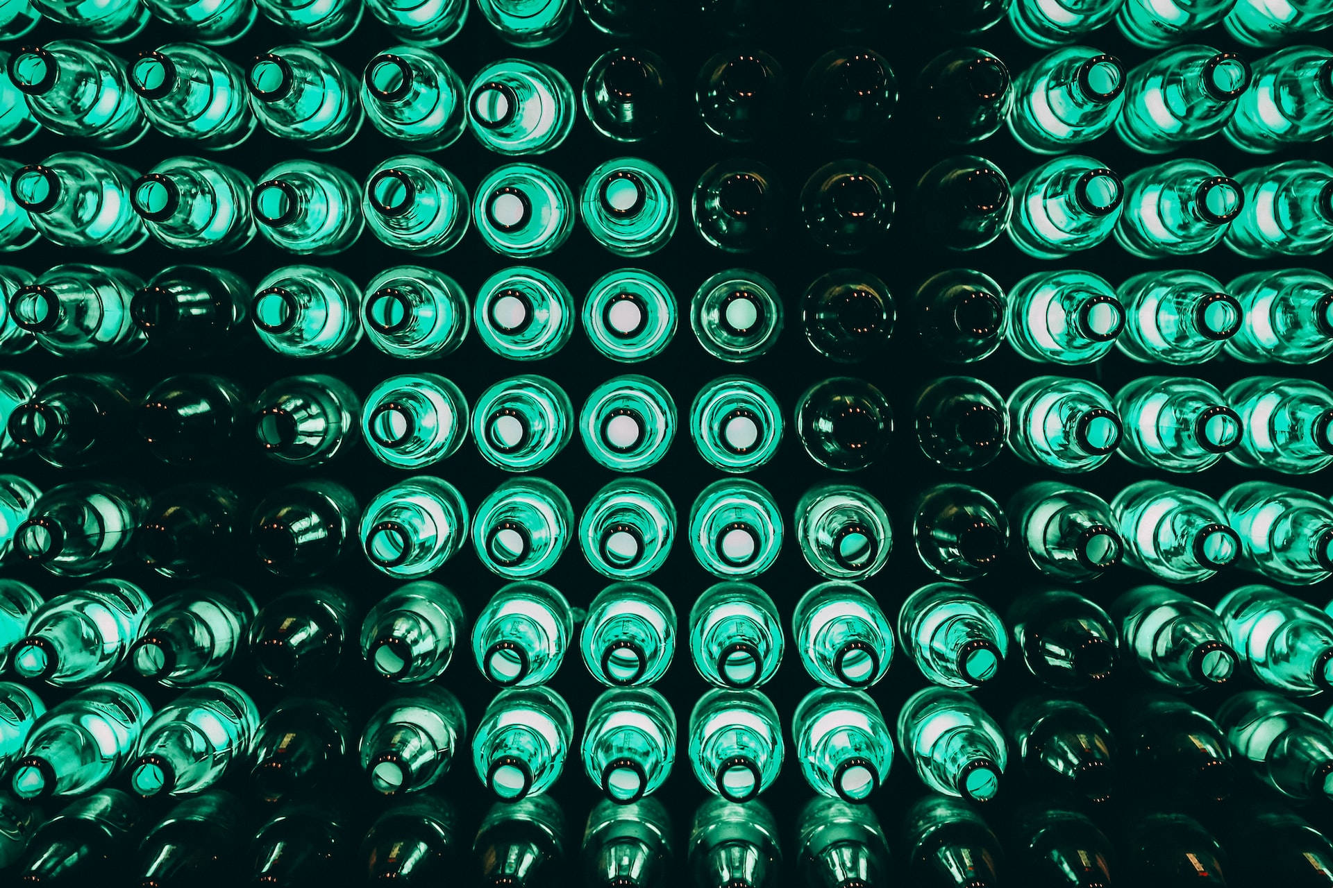 Drink 桌布 壁紙 — 一排排綠色玻璃瓶在黑暗背景下發出霓虹光芒，營造出催眠般的圖案。