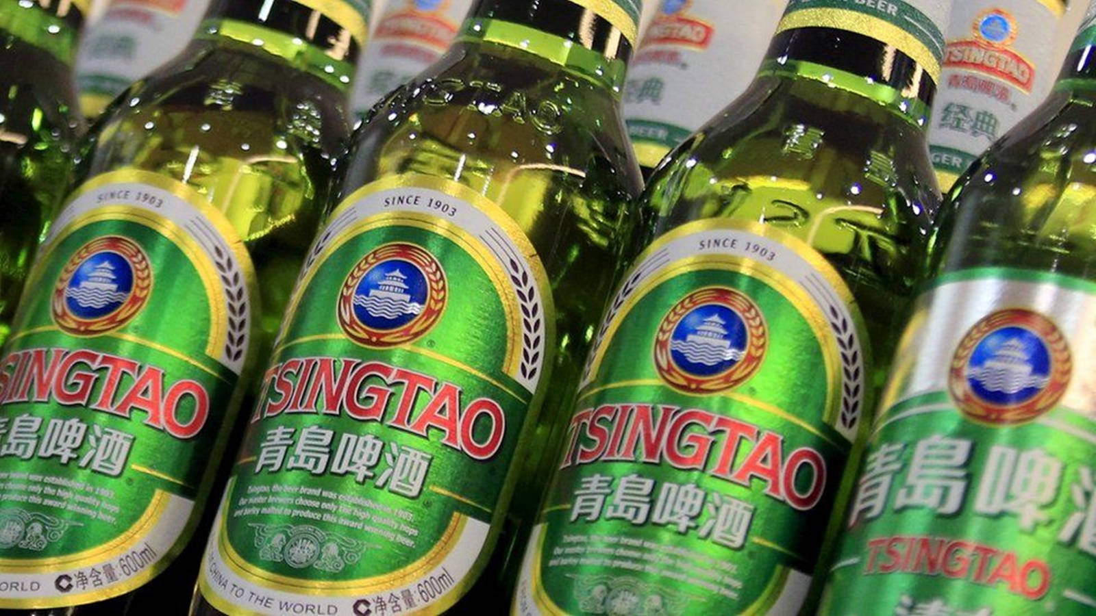 booze 桌布 壁紙 — 一排排綠色青島啤酒瓶，帶有金色和紅色標籤，在明亮的商店燈光下閃閃發光。