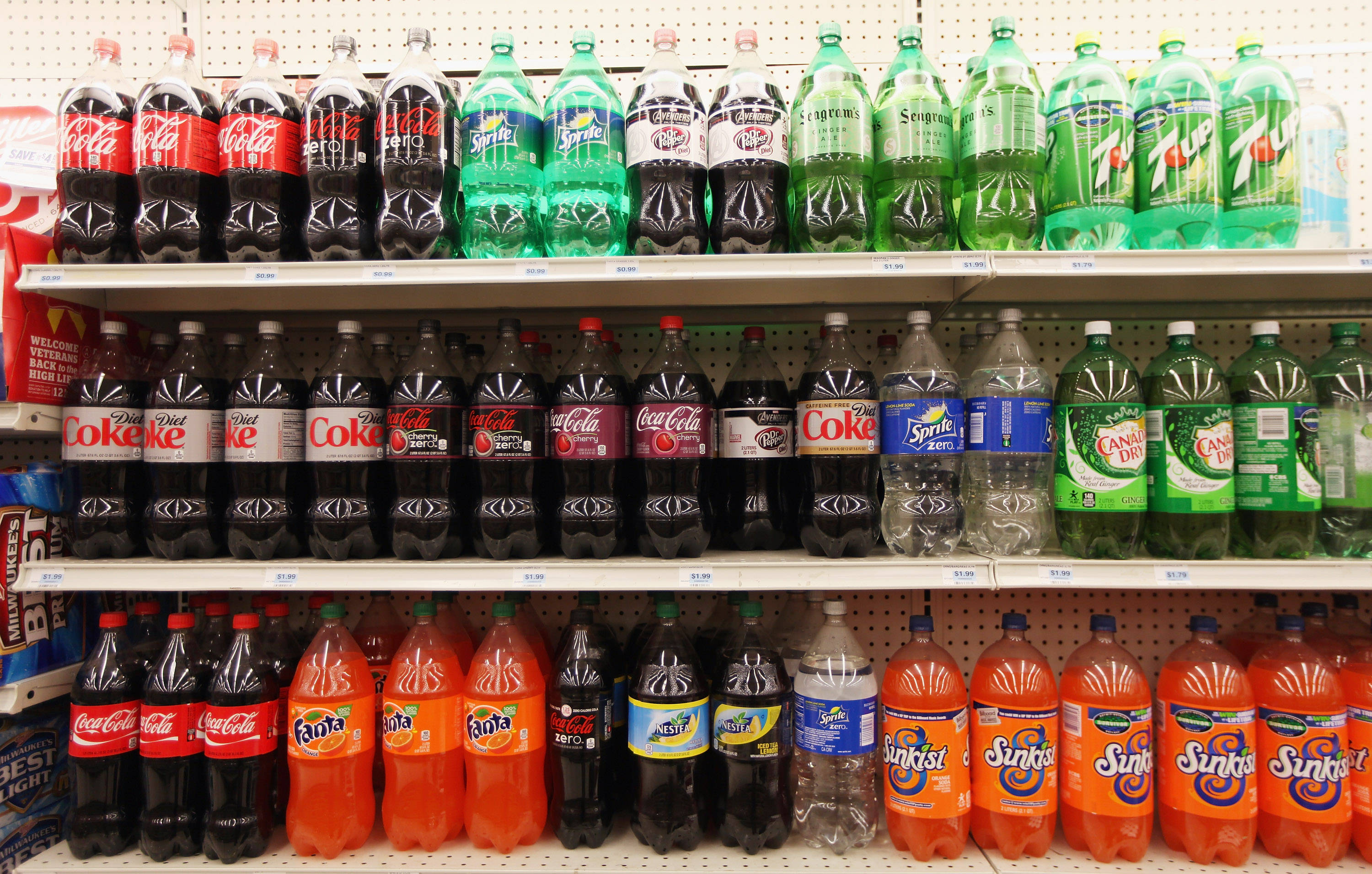 drinks 桌布 壁紙 — 一排排色彩繽紛的汽水瓶整齊地排列在商店貨架上，展示可口可樂、雪碧、七喜、芬達和Sunkist品牌。
