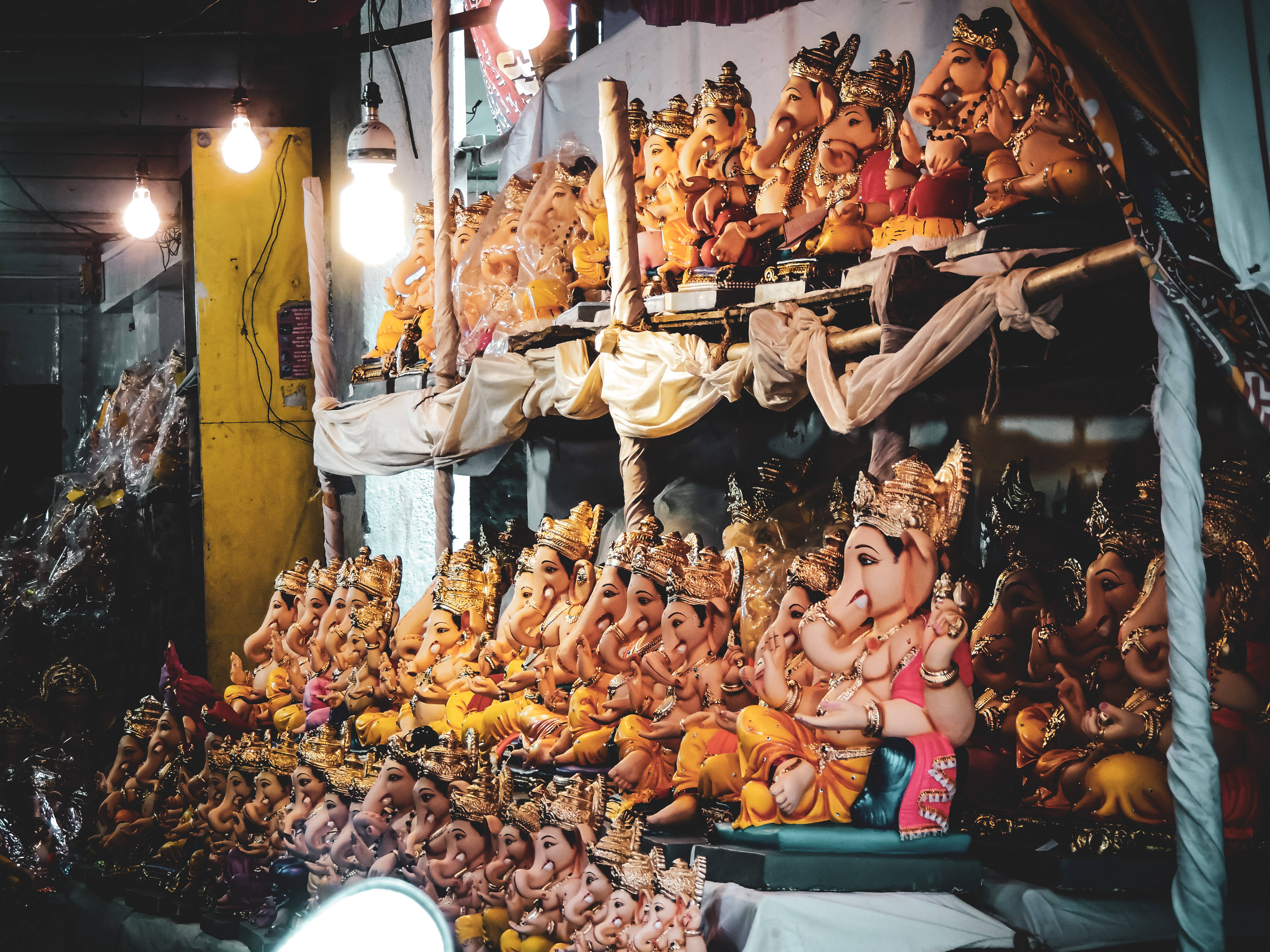 Bappa 桌布 壁紙 — 一排排色彩繽紛的象神雕像在熙熙攘攘的寺廟市場攤位中，在明亮的燈泡下閃閃發光。