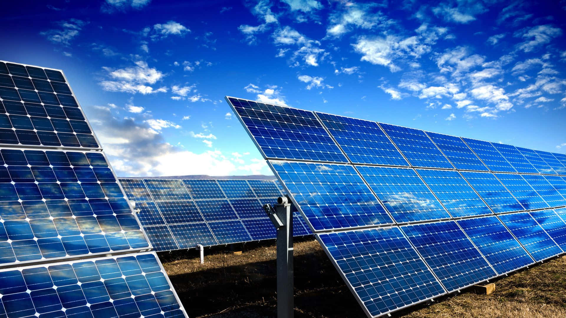 Solar Panel 桌布 壁紙 — 一排排藍色太陽能板在晴朗的日光下反射出明亮的藍天，天空中有零星的白雲。