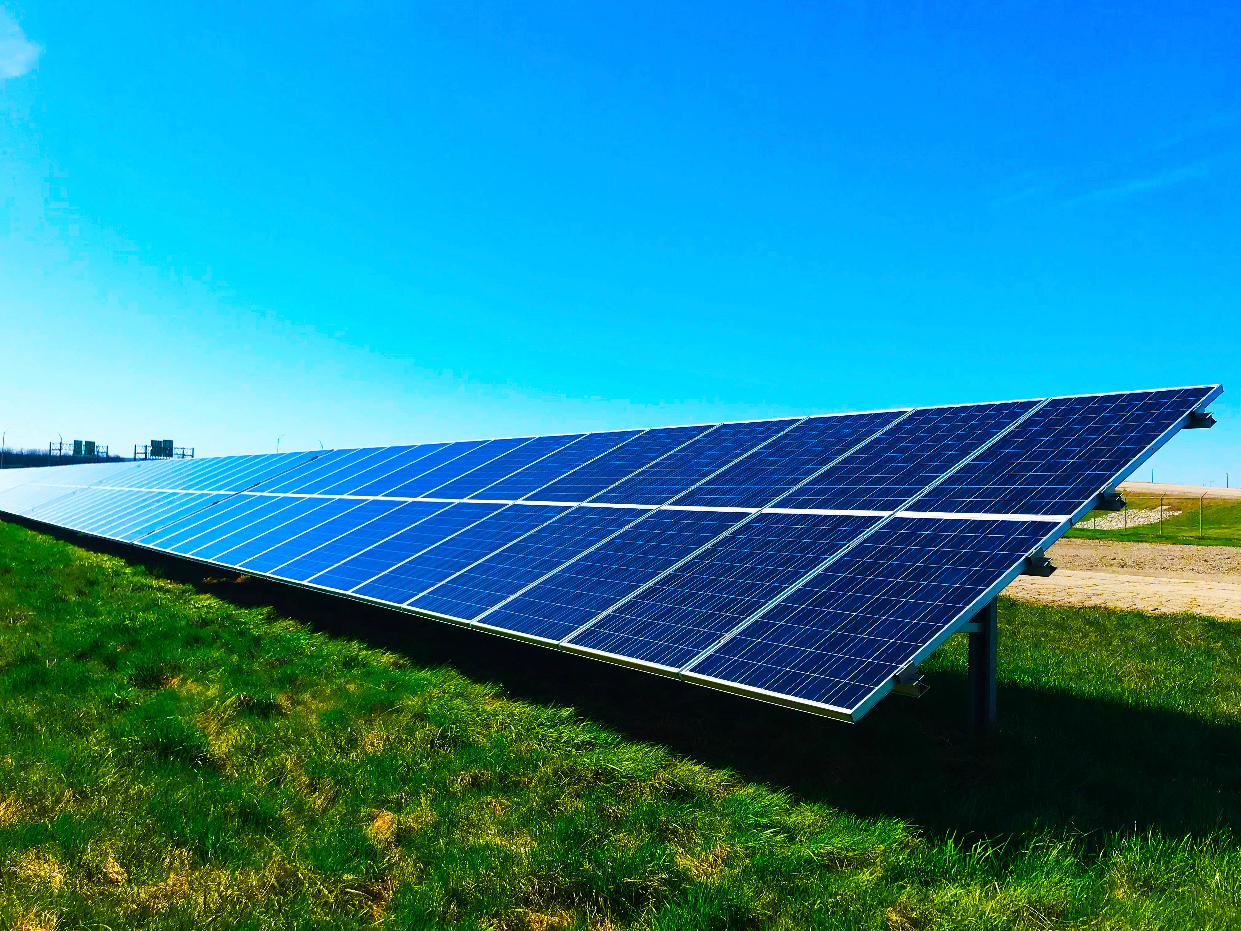Energy 桌布 壁紙 — 一排排藍色太陽能板在晴朗的藍天下在草地上閃閃發光。