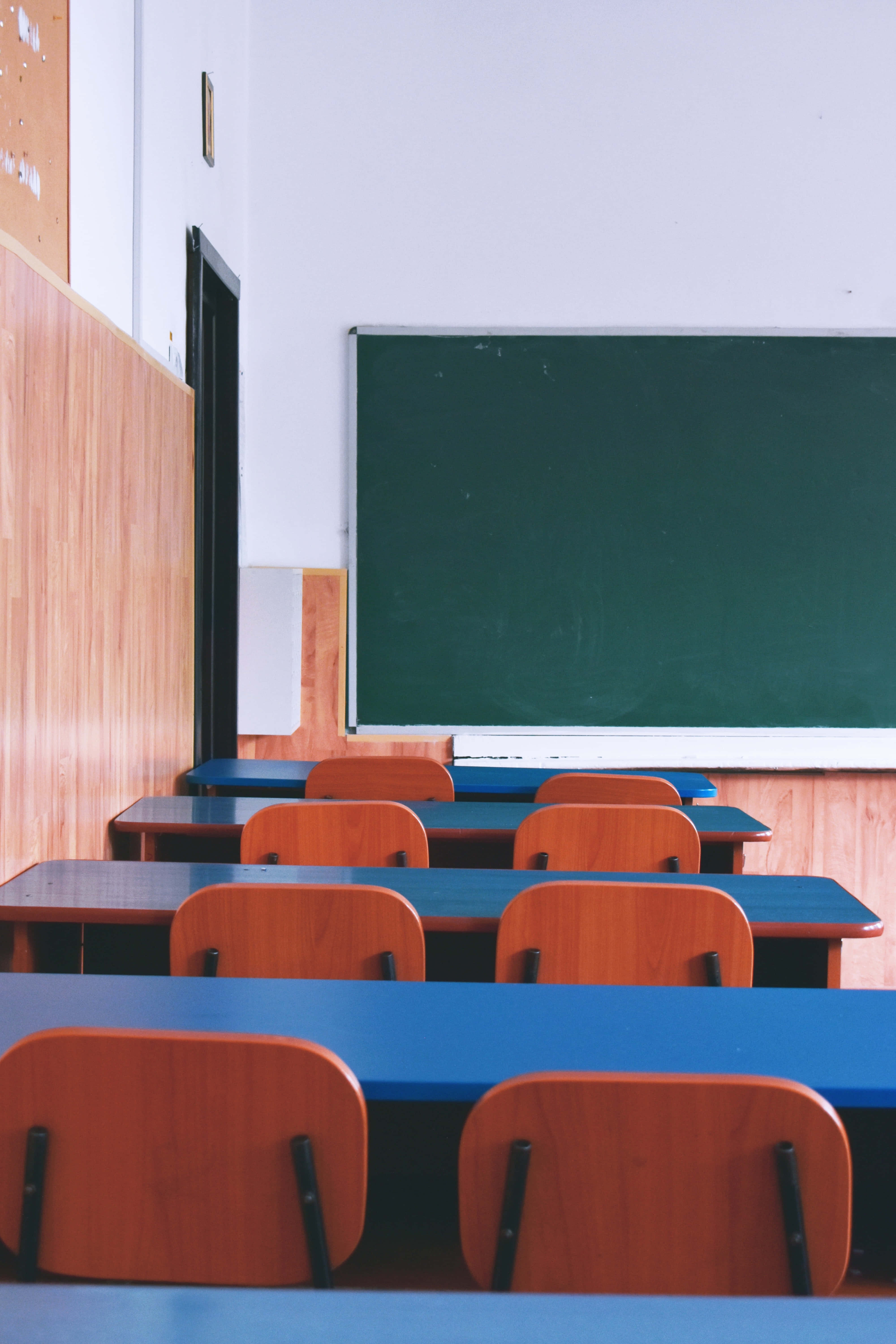 Classroom 桌布 壁紙 — 一排排藍色書桌和木椅面向綠色黑板，位於空無一人的教室，牆壁是淺色木鑲板。
