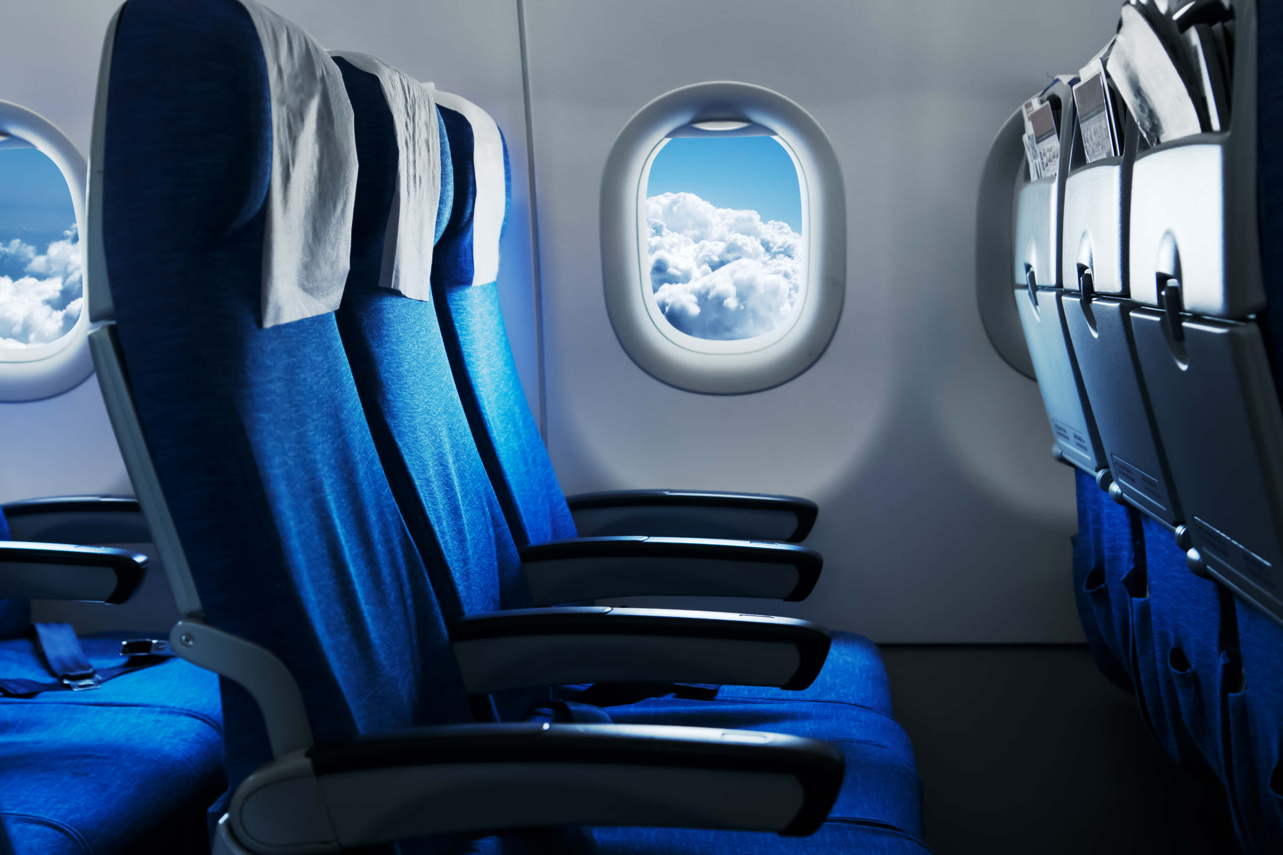 Airplane Window 桌布 壁紙 — 一排排藍色飛機座位面向窗戶，窗外是明亮藍天下蓬鬆的白雲。