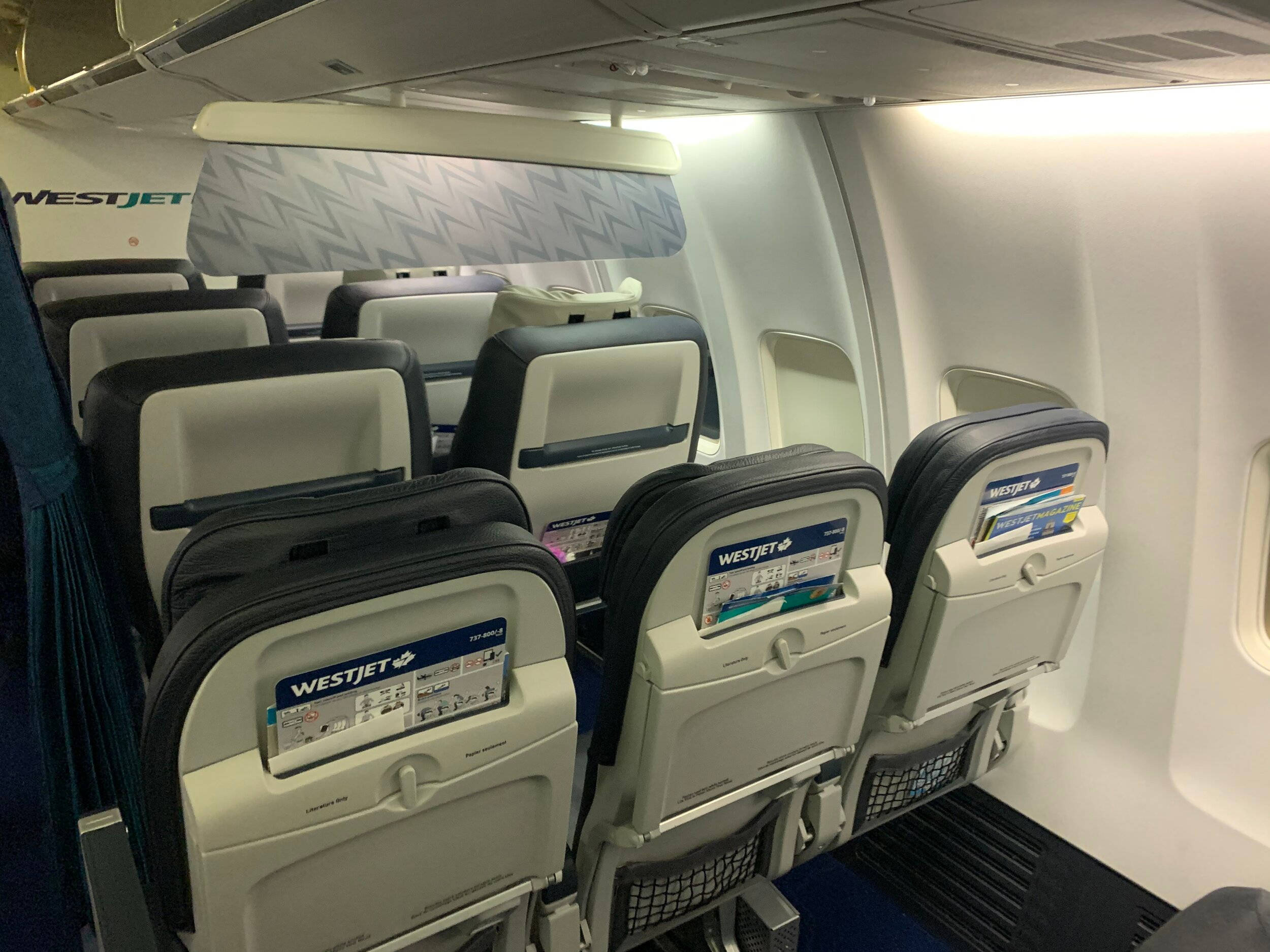 seat 桌布 壁紙 — 一排排西捷航空飛機座位，配有頭頂行李艙和安全卡，機艙內部乾淨整潔。