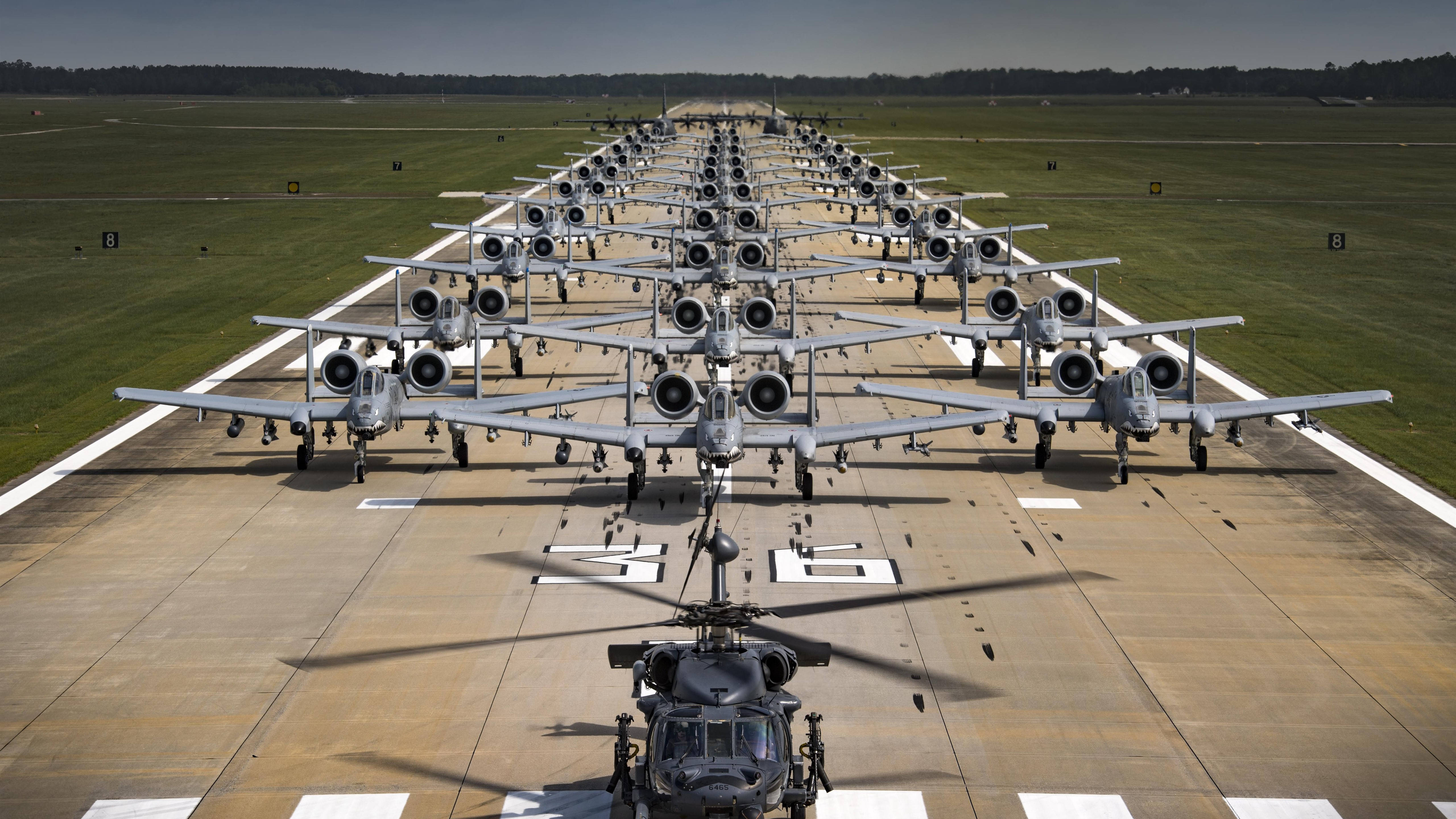 Airport 桌布 壁紙 — 一排排軍用攻擊機排列在停機坪上，前景有一架直升機，天空晴朗。