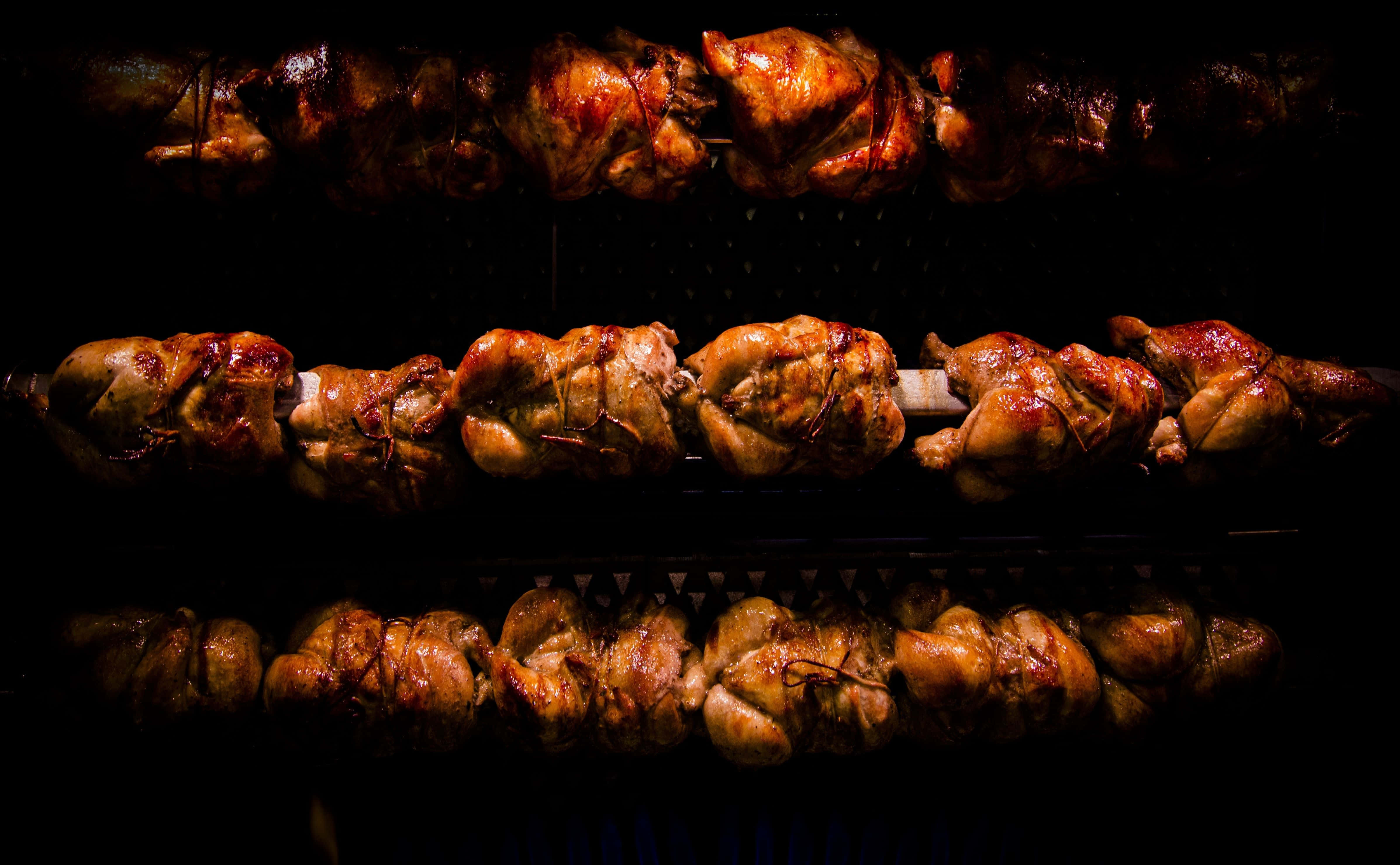 Bbq 桌布 壁紙 — 一排排閃亮的烤雞在金屬桿上旋轉，背景漆黑一片。