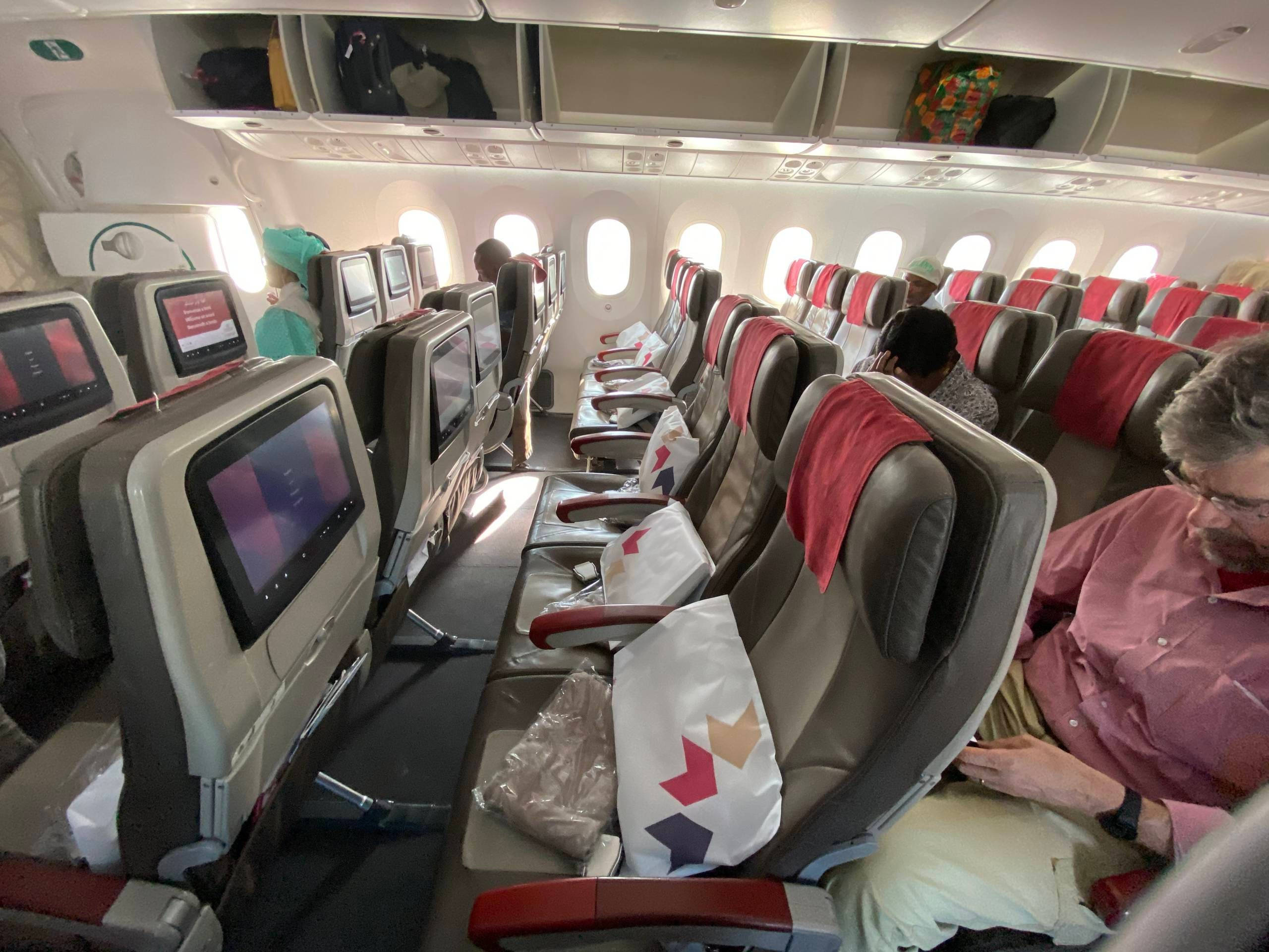飛機 桌布 壁紙 — 一排排飛機座位，乘客正在休息，個人螢幕在明亮的機艙中發光。