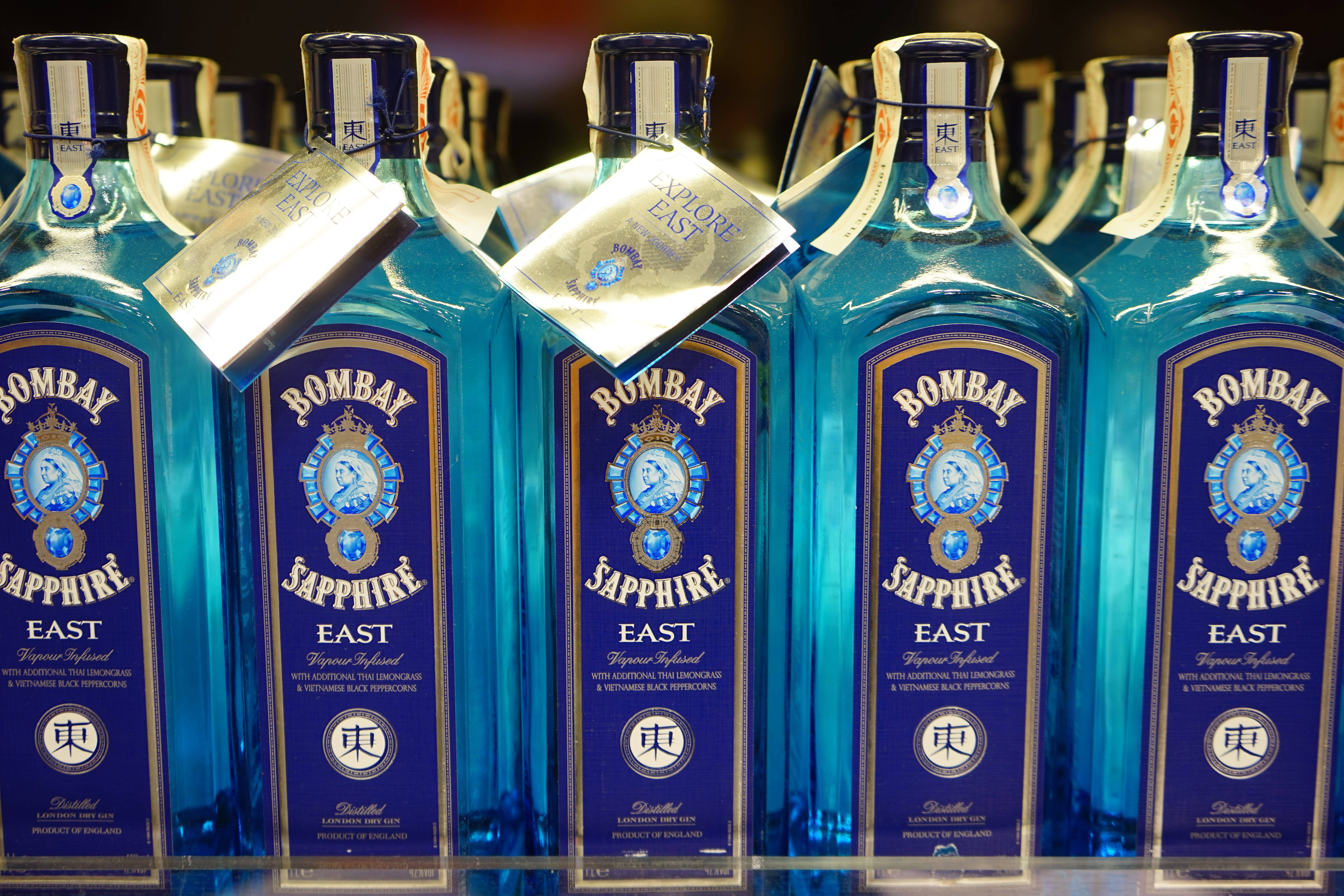 bottle 桌布 壁紙 — 一排排鮮藍色的 Bombay Sapphire East 琴酒瓶，帶有金色標籤和吊牌，在商店中展示。