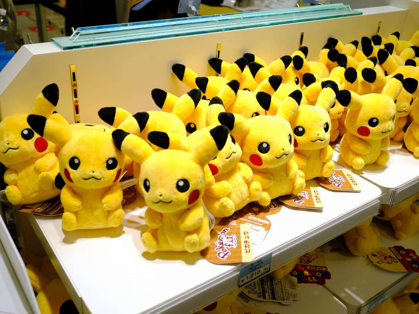Pokemon Toys 桌布 壁紙 — 一排排鮮黃色的皮卡丘毛絨玩具整齊地放在白色商店貨架上，附有價格標籤。