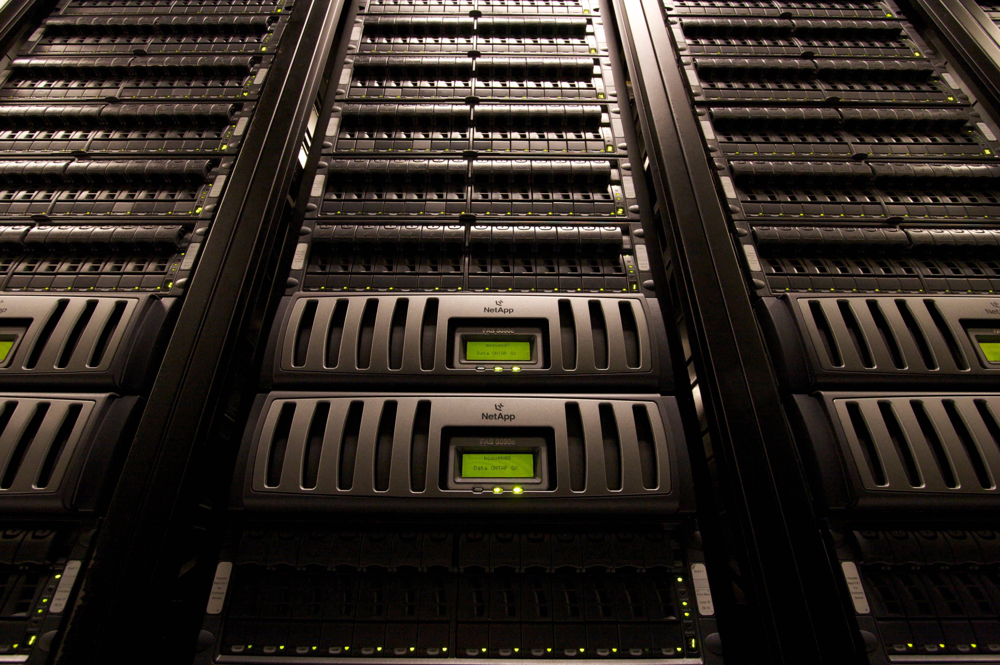 data 桌布 壁紙 — 一排排黑色 NetApp 伺服器機架，在昏暗的資料中心中發出綠色狀態燈光。