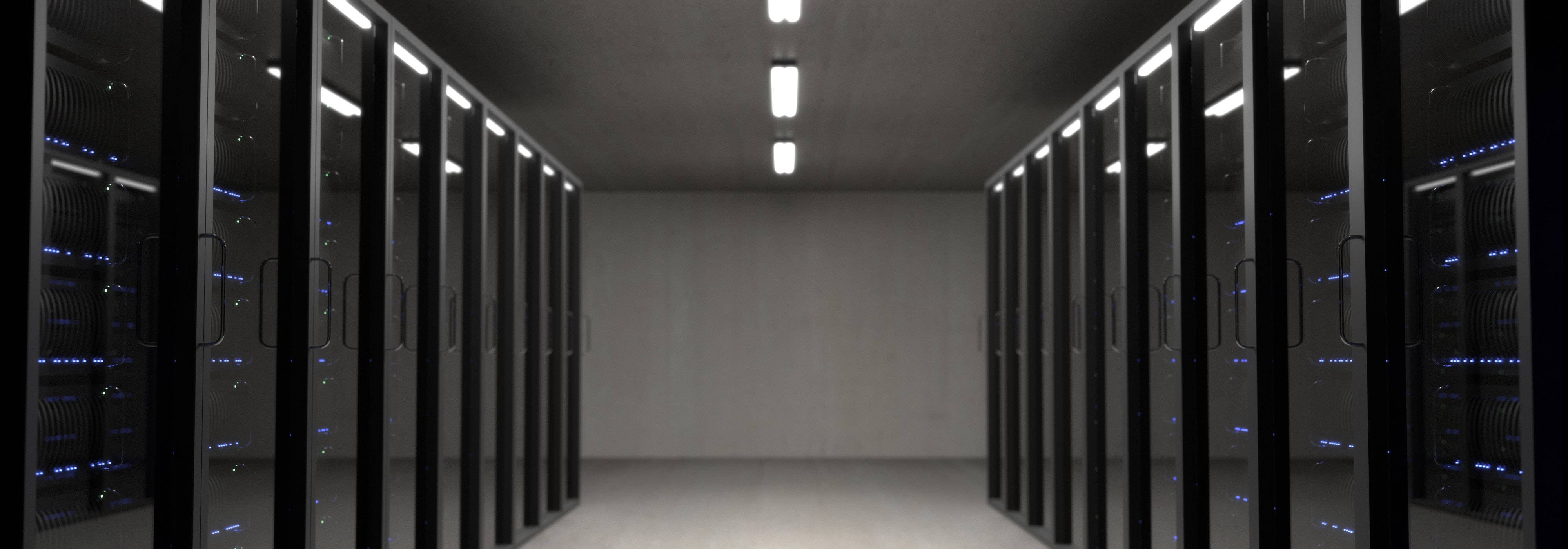 Data Center 桌布 壁紙 — 一排排黑色伺服器機架，帶有發光的藍色燈光，排列在一條簡樸的混凝土資料中心走廊中。
