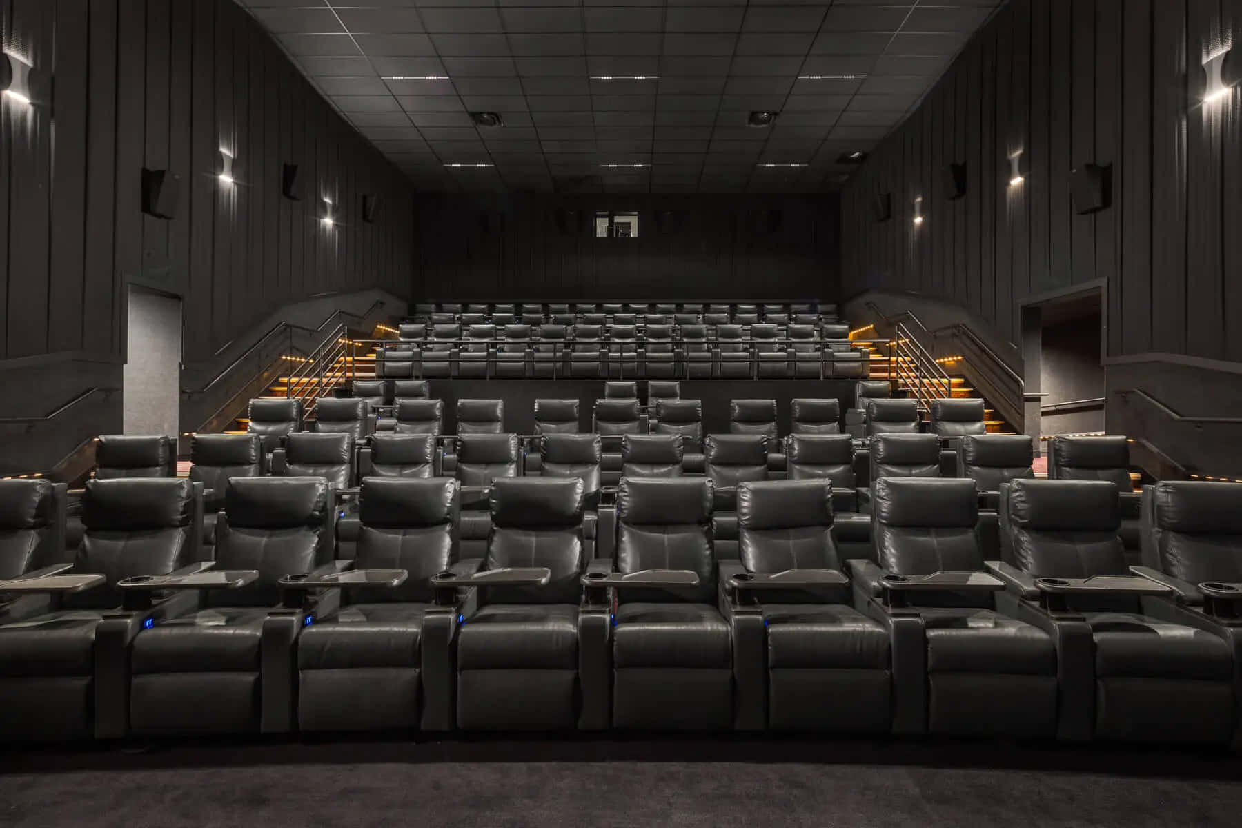 Movie Theater 桌布 壁紙 — 一排排黑色皮革躺椅充滿了光線昏暗的現代電影院，樓梯上設有溫暖的氛圍燈光。
