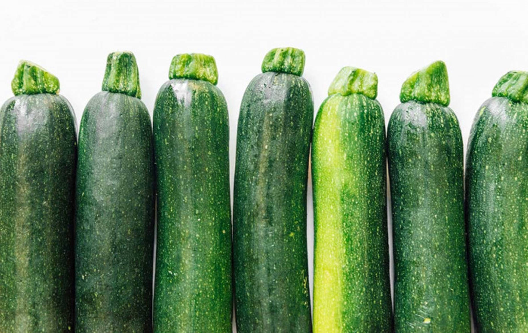 Vegetables 桌布 壁紙 — 一排新鮮的綠色櫛瓜，帶有露珠，整齊排列在潔白的背景上。