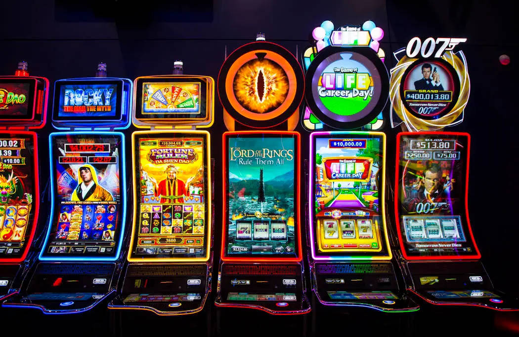 Arcade Aesthetic 桌布 壁紙 — 一排明亮照明的賭場老虎機，在黑暗的房間中閃爍著色彩繽紛的主題，如詹姆士·龐德和魔戒。