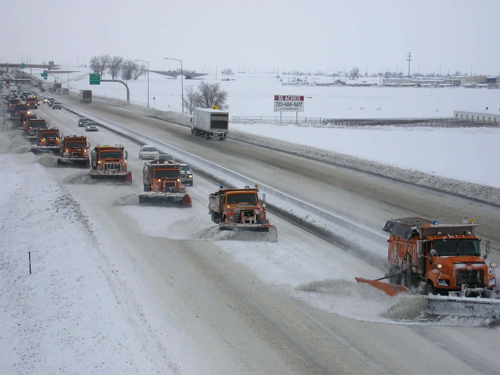 Snowplow 桌布 壁紙 — 一排橙色掃雪車在多雲的冬日天空下清理多車道高速公路上的積雪。