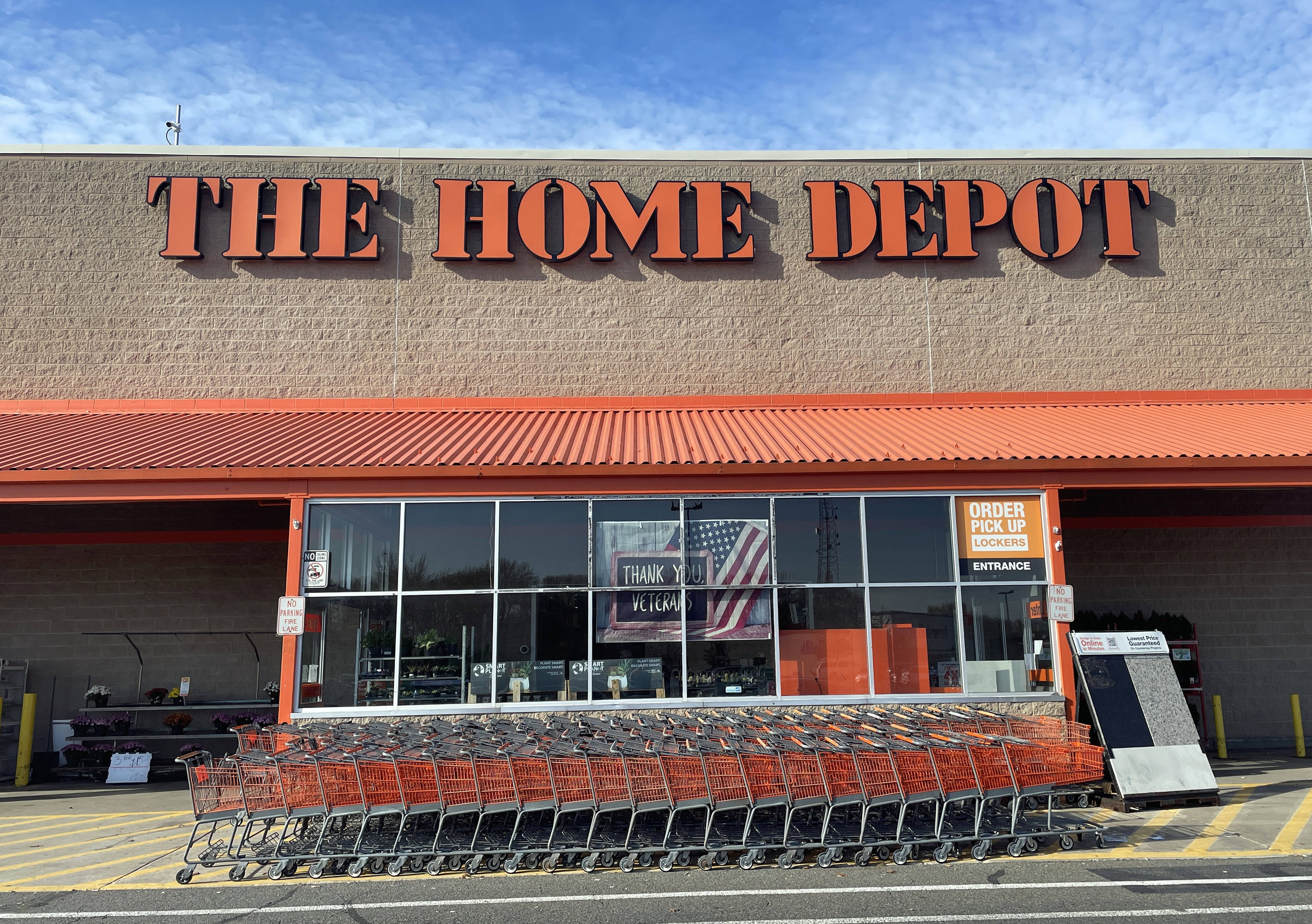 Home Depot 桌布 壁紙 — 一排橙色購物車排列在Home Depot商店入口處，上方是晴朗的藍天，點綴著幾朵白雲。