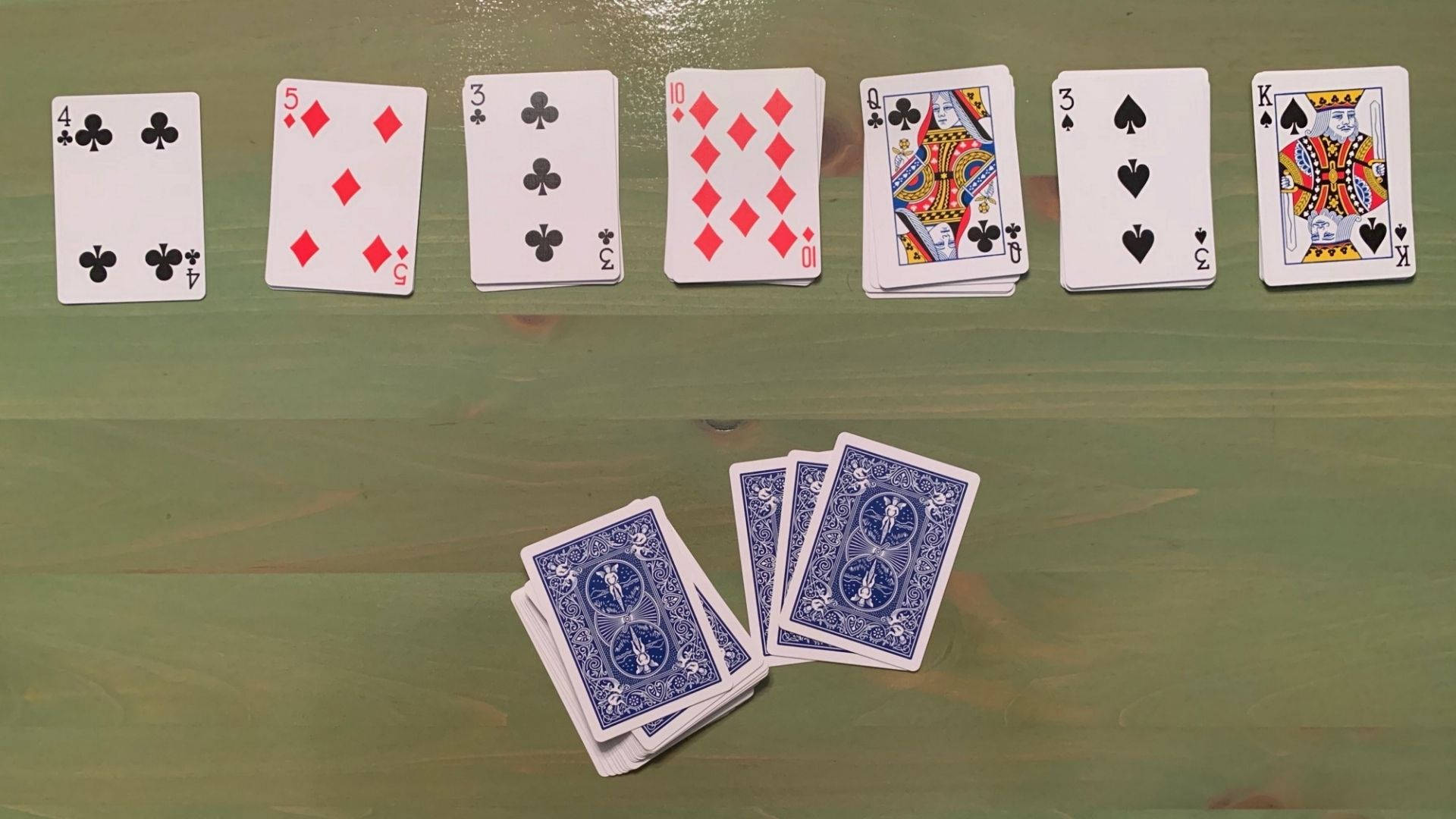 Solitaire 桌布 壁紙 — 一排正面朝上的撲克牌放在綠色木質表面上，附近有一小疊背面朝上的撲克牌。
