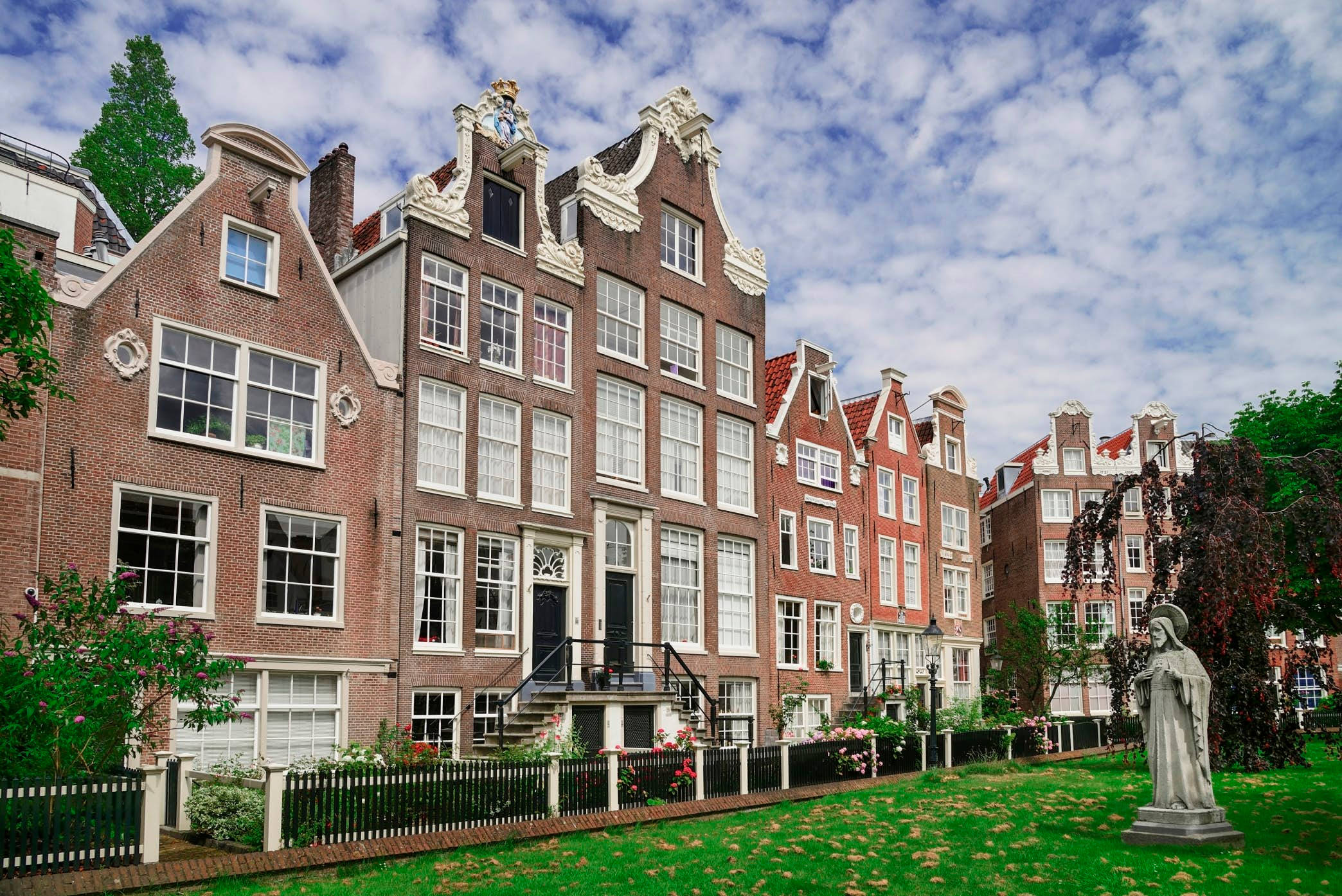 Amsterdam 桌布 壁紙 — 一排歷史悠久的荷蘭運河房屋，擁有山形屋頂和白色框架窗戶，天空部分多雲。