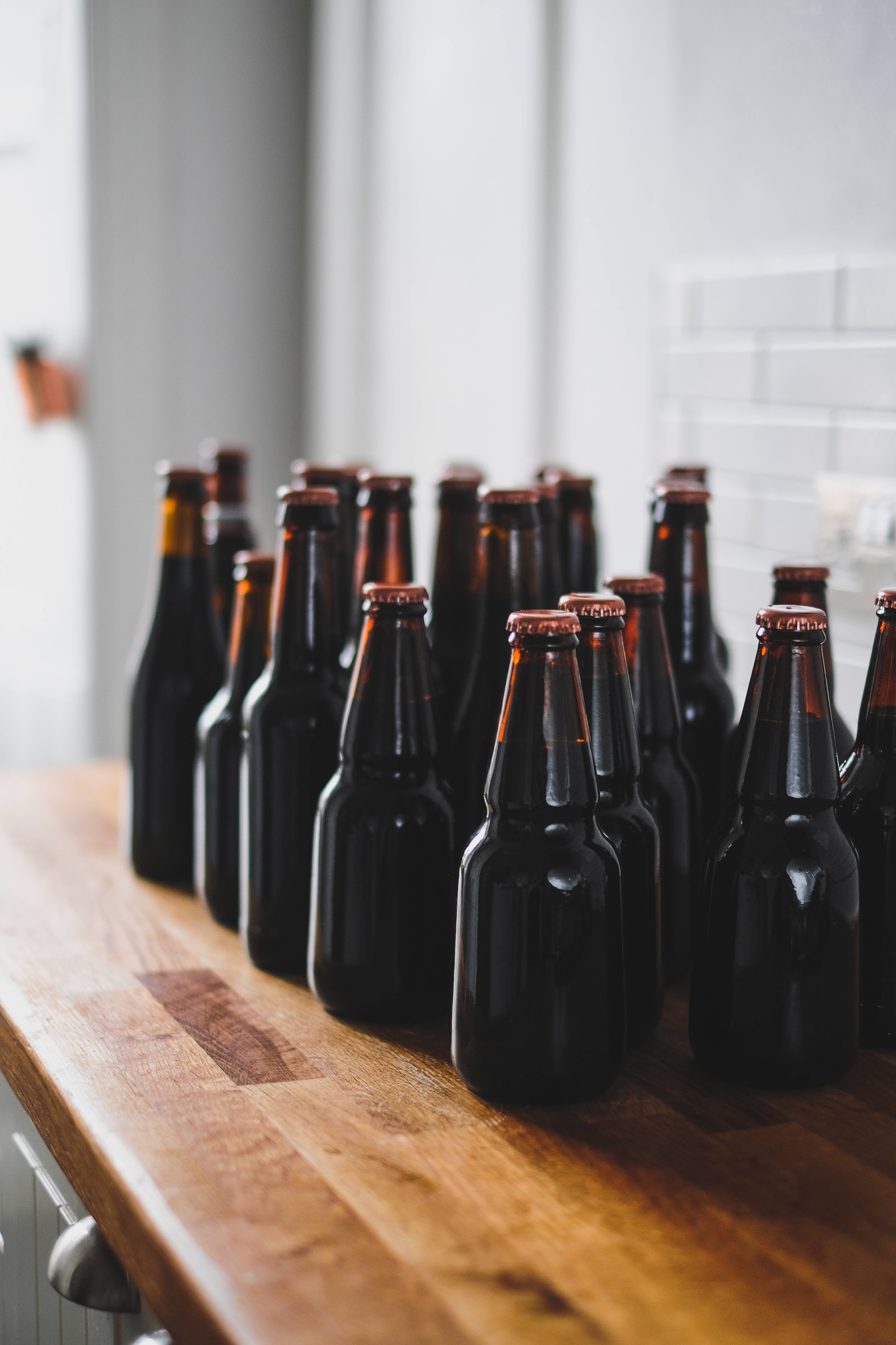 Beer 桌布 壁紙 — 一排深琥珀色啤酒瓶，帶銅色瓶蓋，整齊地放在明亮廚房的溫暖木質檯面上。