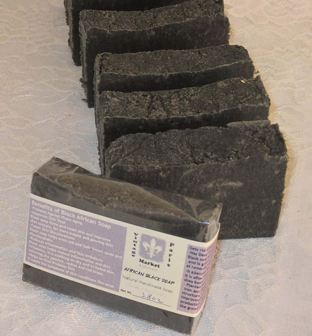 Black Soap 桌布 壁紙 — 一排深色紋理非洲黑皂條，標籤詳細說明功效和淨重，排列在淺色圖案表面上。