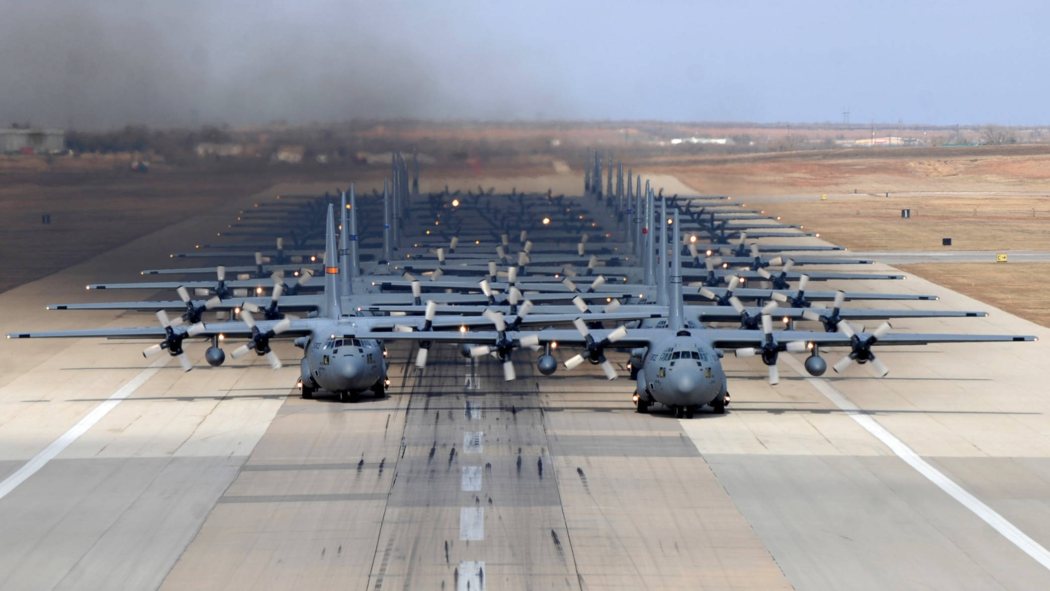 Runway 桌布 壁紙 — 一排灰色軍用運輸機排列在跑道上，天空朦朧，遠處有煙霧。