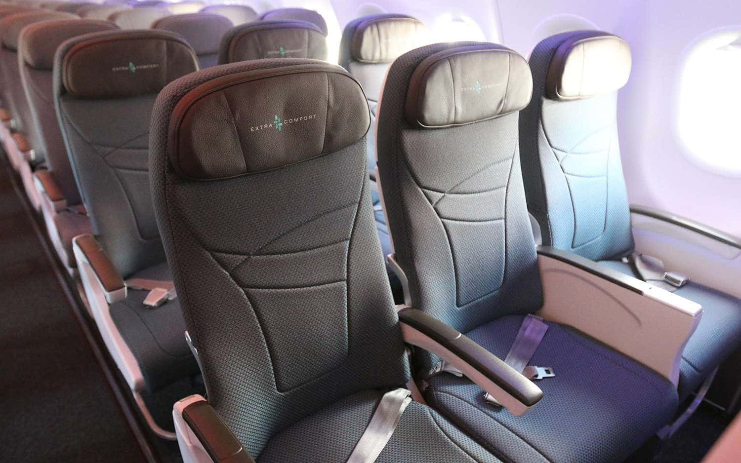 飛機 桌布 壁紙 — 一排現代飛機座椅，帶有「額外舒適」品牌和藍色軟墊，位於窗邊柔和的機艙燈光下。