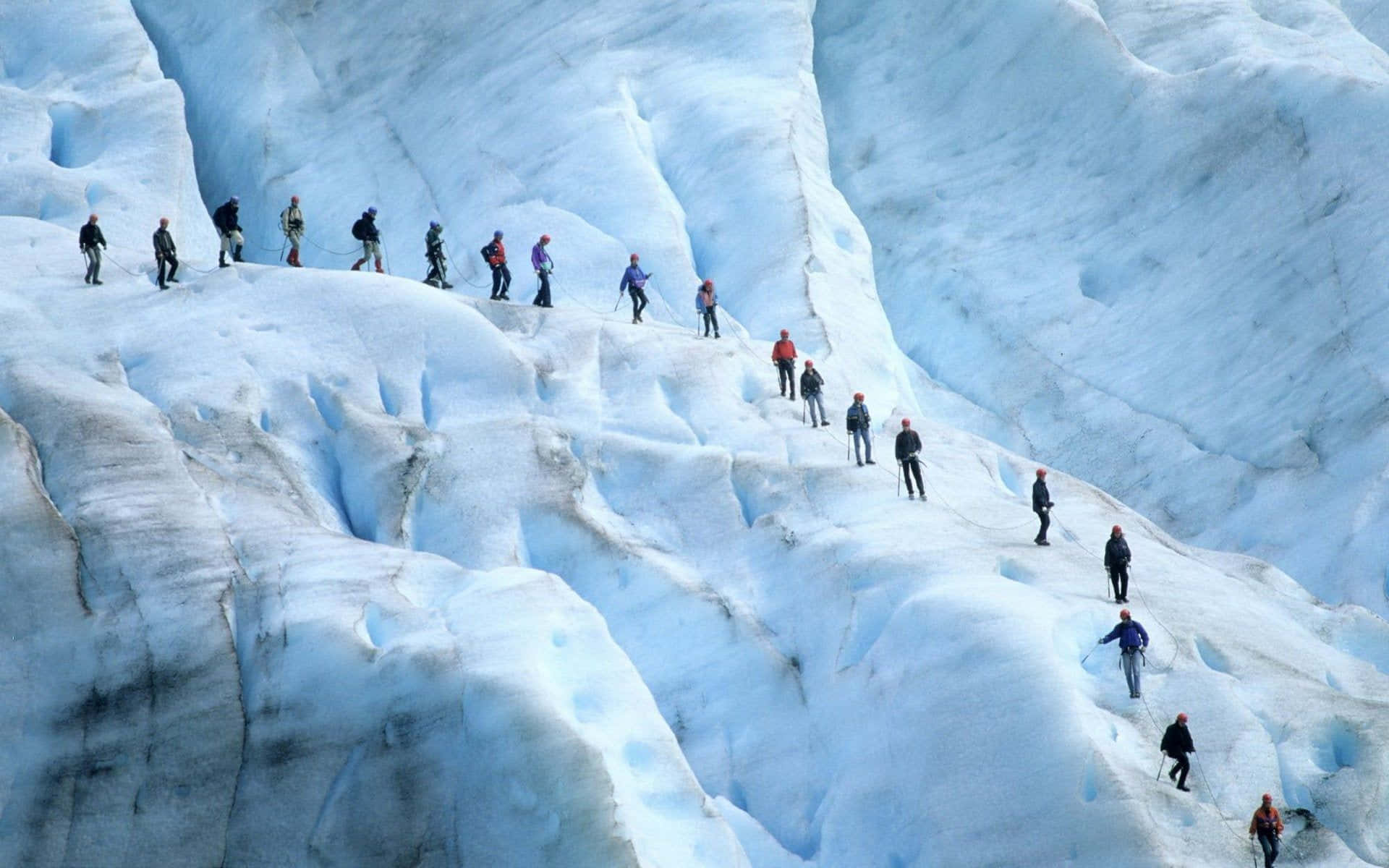Ice Climbing 桌布 壁紙 — 一排登山者在明亮的日光下攀登一座擁有深藍色冰層和崎嶇裂縫的巨大冰川。