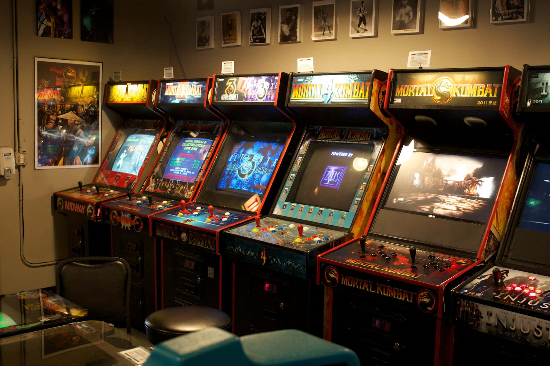 桌布 壁紙 — 一排發光的 Mortal Kombat 街機排列在燈光昏暗的復古遊戲室中，牆上貼有海報。