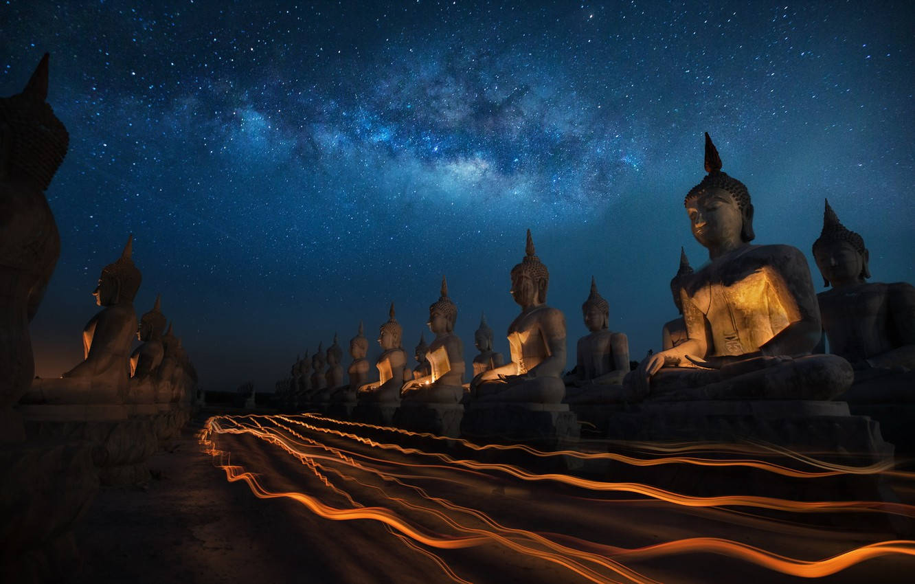 god laptop 桌布 壁紙 — 一排發光的佛像，在繁星點點的夜空下，銀河拱起，下方有發光的橙色光跡。