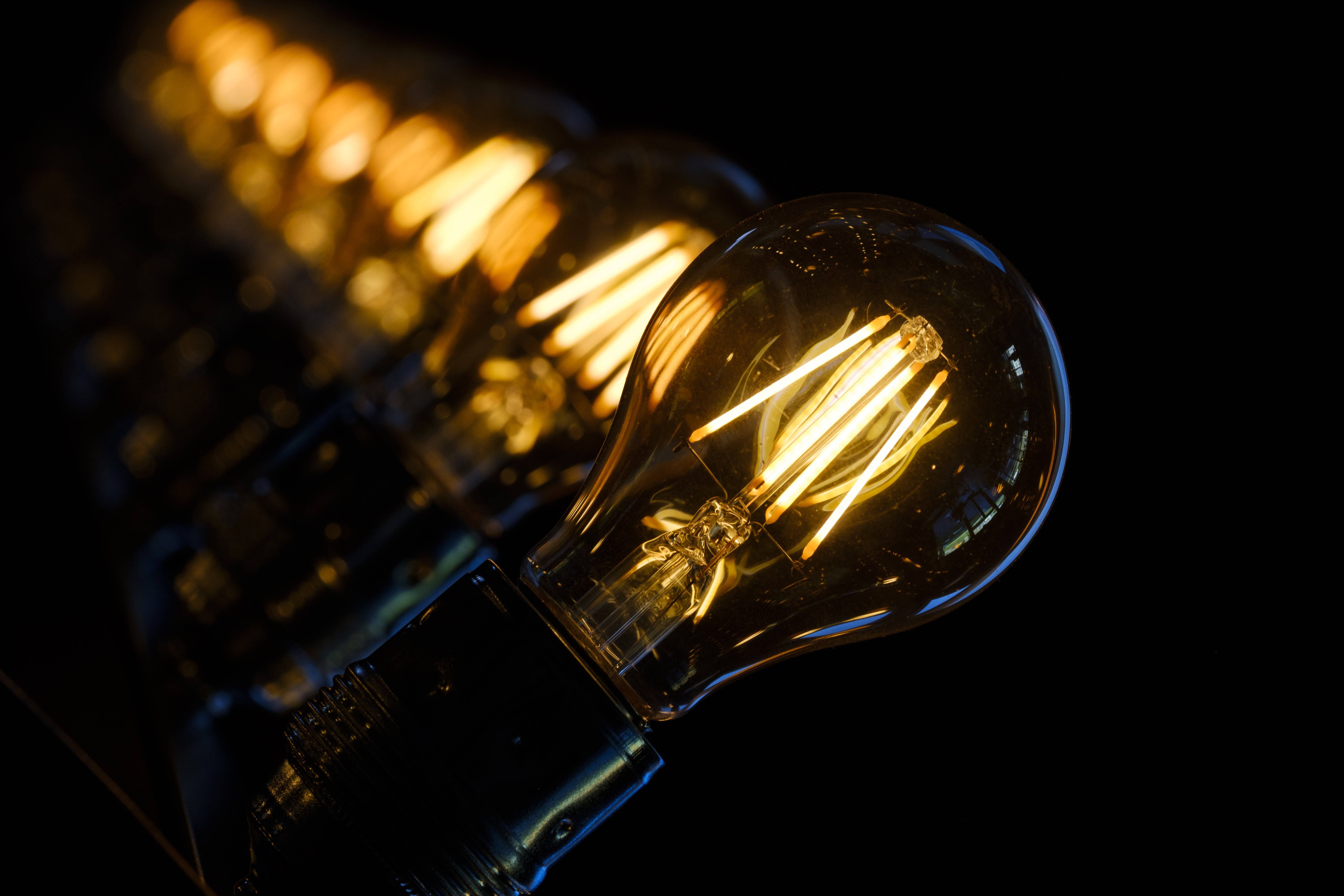 Light Bulb 桌布 壁紙 — 一排發光的復古燈絲燈泡，在深黑色背景上發出溫暖的金色光芒。
