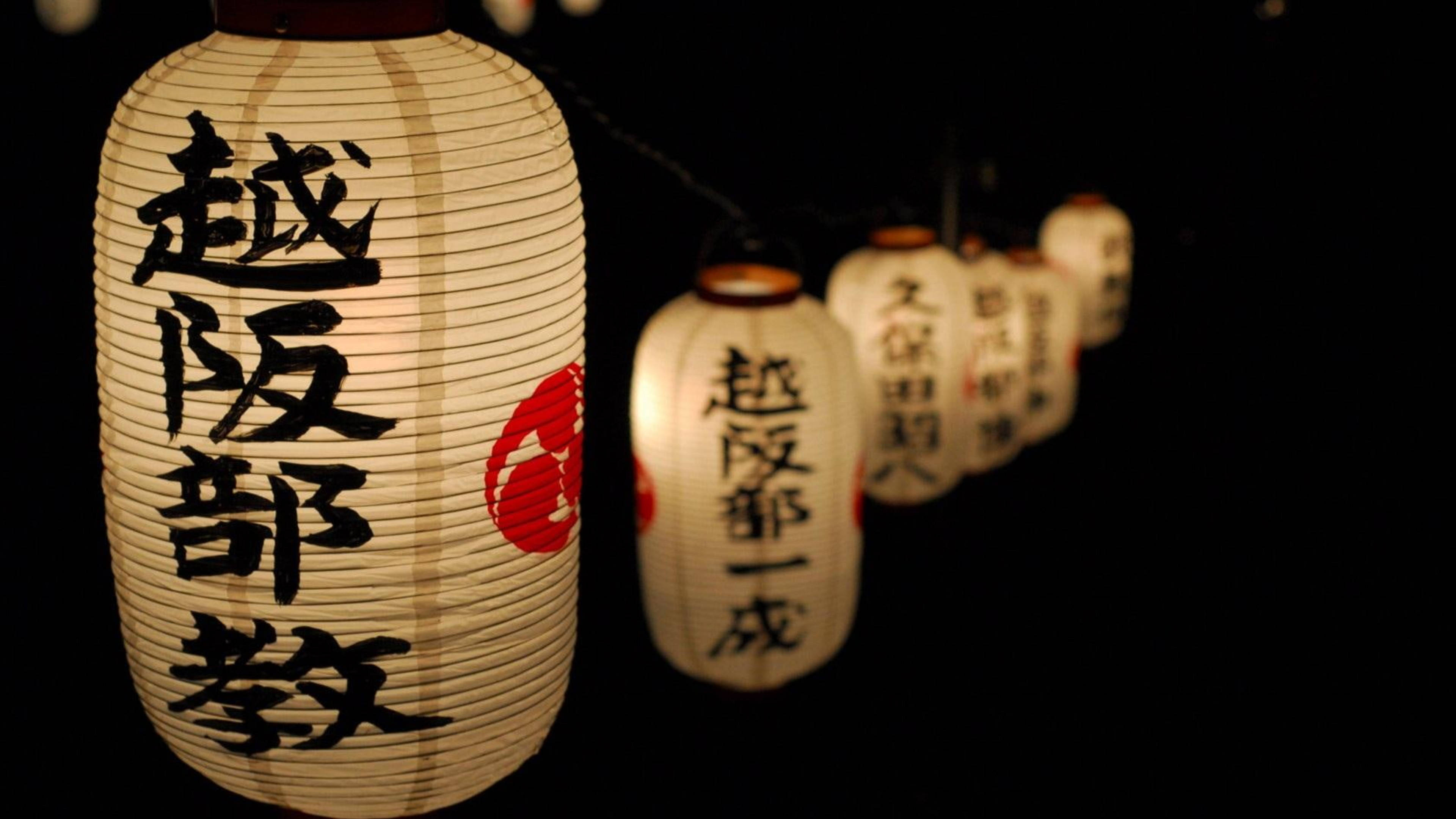 日式 桌布 壁紙 — 一排發光的日本紙燈籠，帶有黑色書法和紅色印章，照亮了黑暗的夜景。