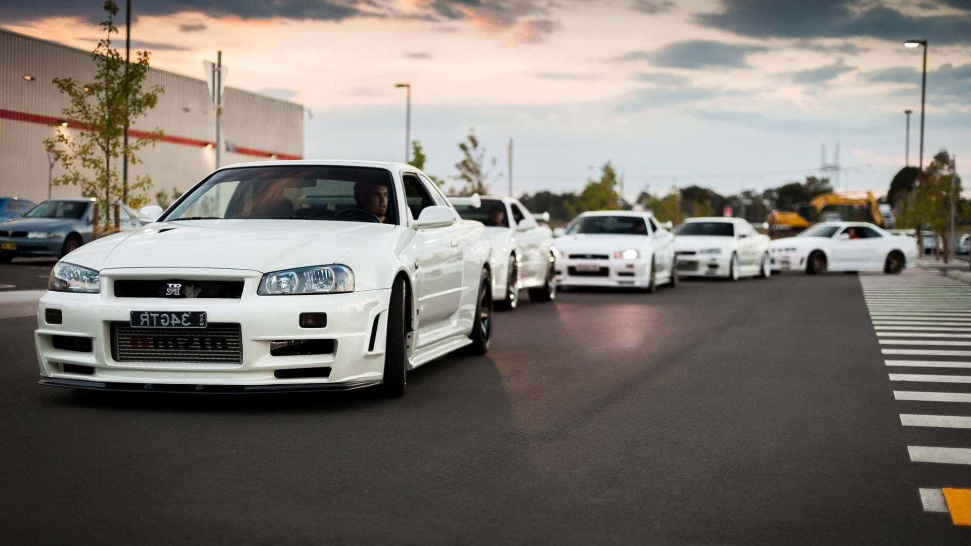 JDM汽車 桌布 壁紙 — 一排白色日產Skyline GT-R停放在瀝青場地上，天空多雲，暮色蒼茫。