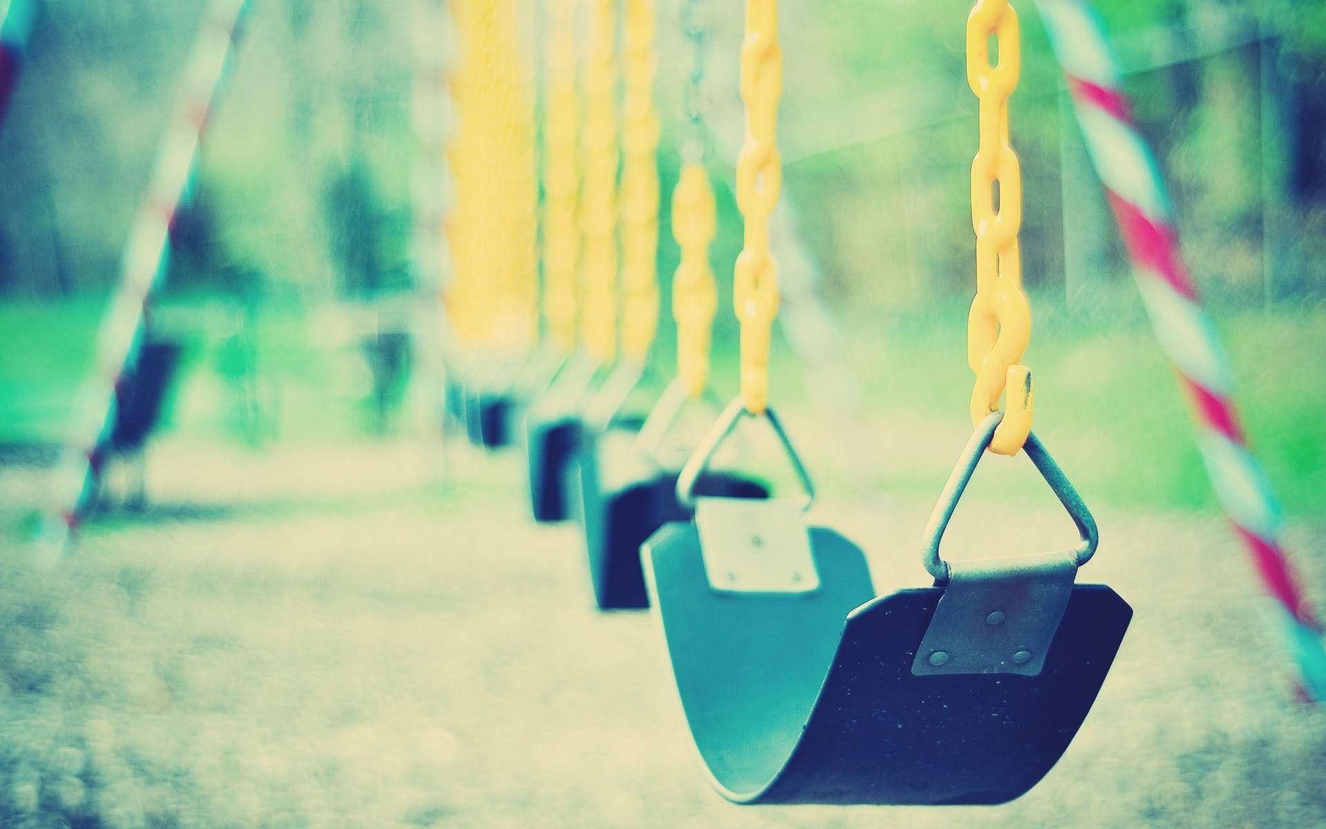 Playground 桌布 壁紙 — 一排空藍色鞦韆配黃色鏈條，在柔和模糊的公園中，在復古色彩濾鏡下懸掛著。
