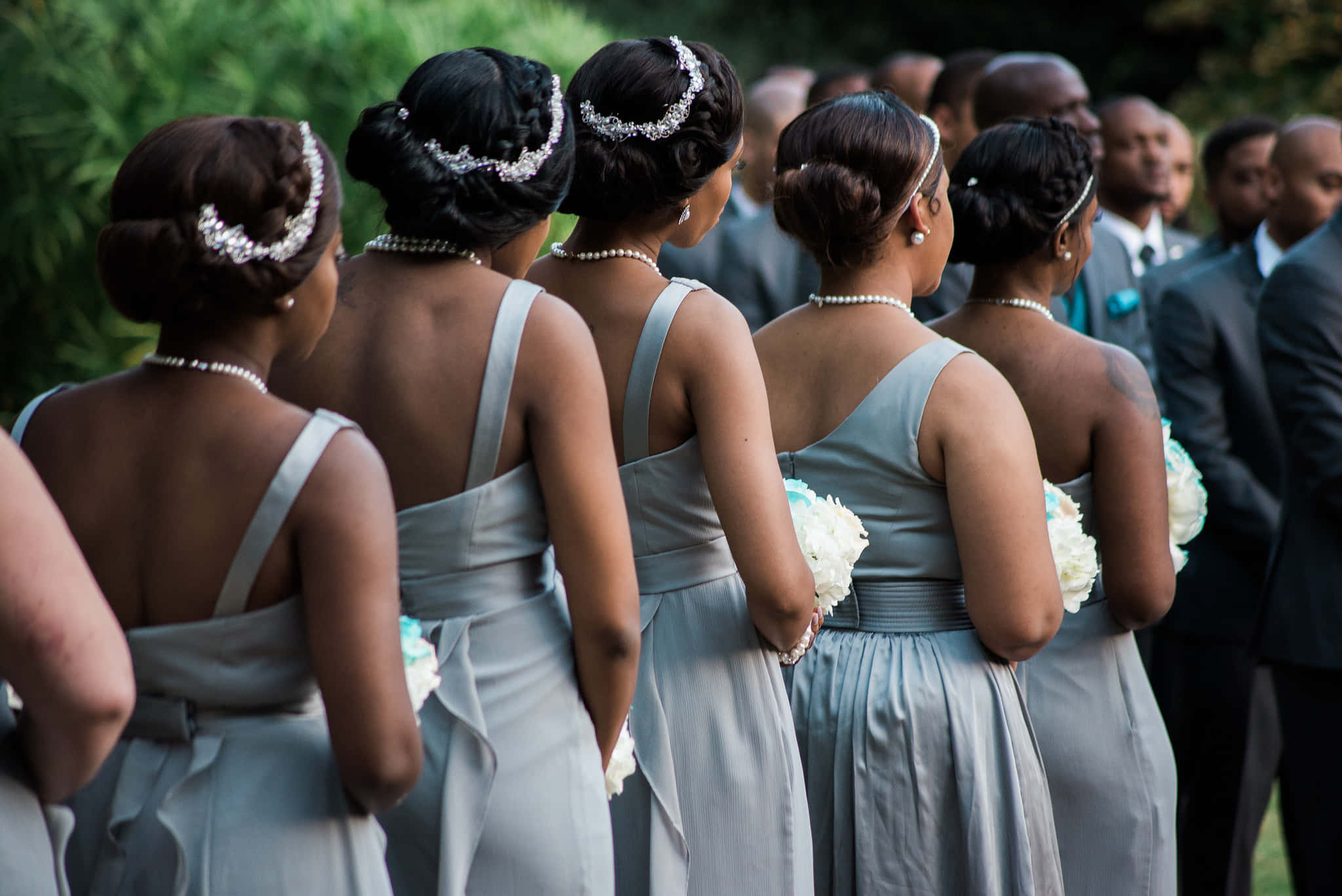Bridesmaids 桌布 壁紙 — 一排穿著優雅銀色禮服和珍珠配飾的伴娘在戶外婚禮上背對鏡頭站立。