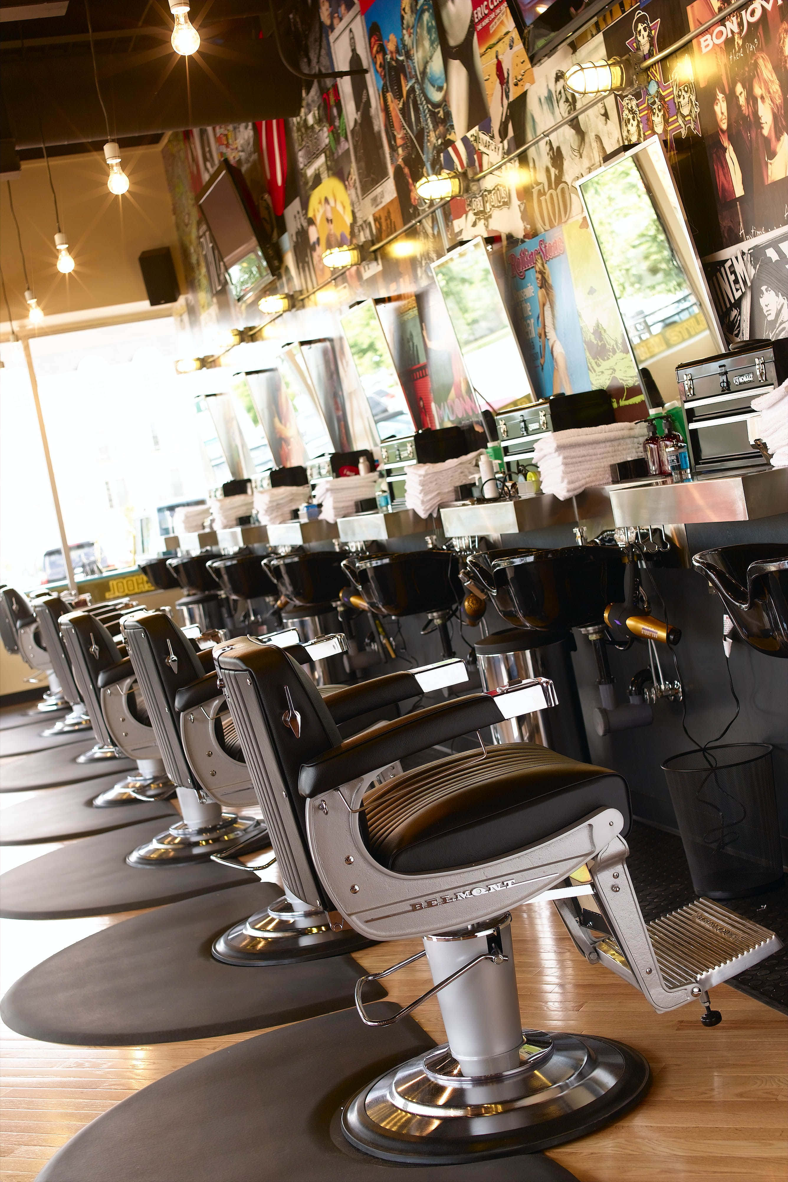 Barber Shop 桌布 壁紙 — 一排經典理髮椅，帶有鍍鉻底座和黑色皮革座椅，排列在一間充滿活力的理髮店中，店內裝飾著漫畫海報和明亮的頂燈。