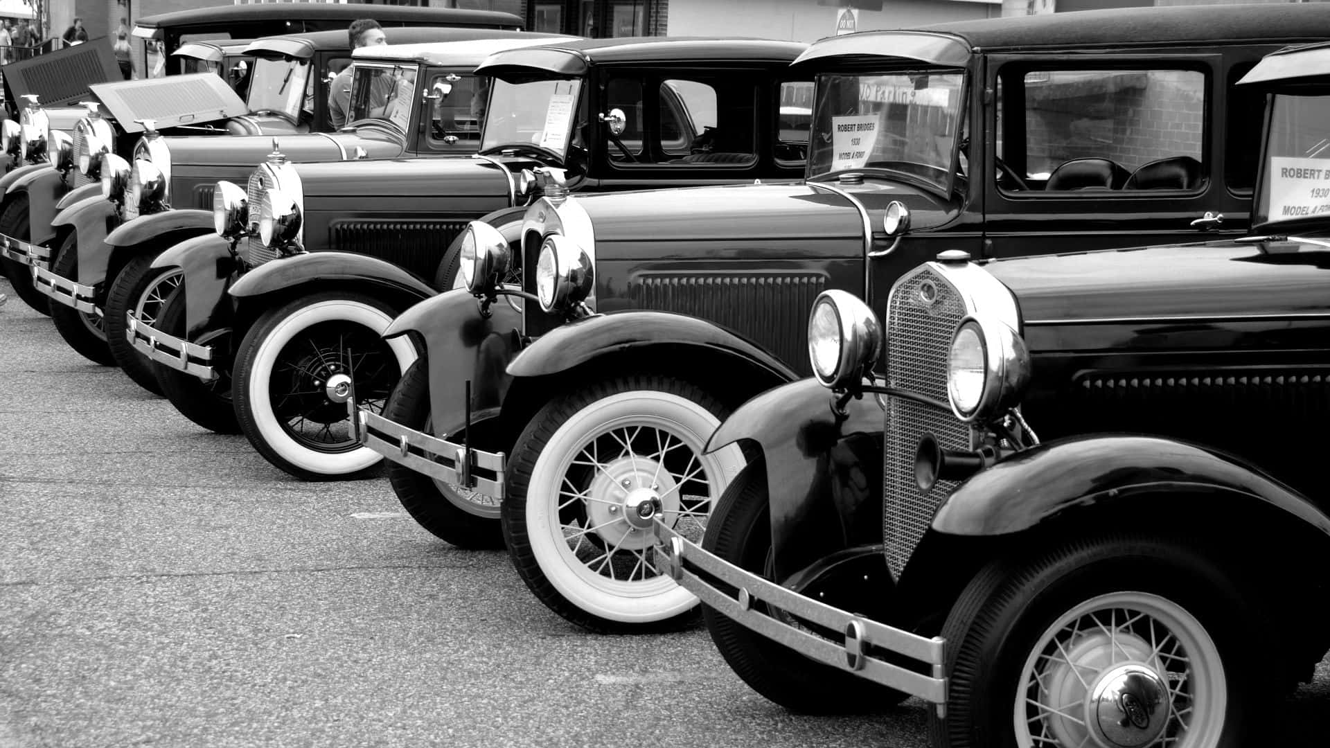 Black And White Vintage Car 桌布 壁紙 — 一排經典黑色老爺車配白色側壁輪胎，停泊在黑白瀝青路上。