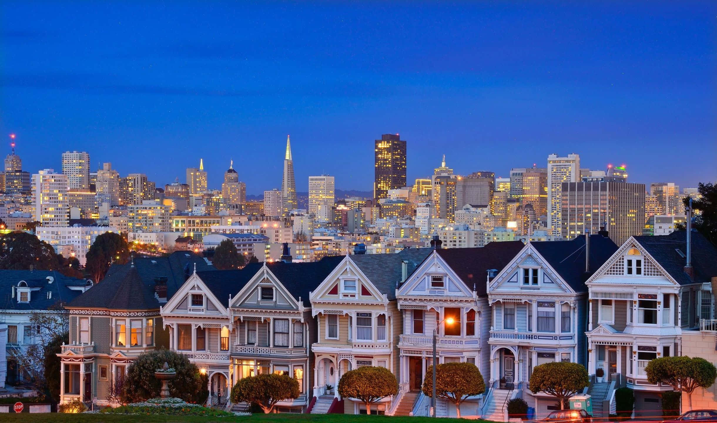 2440x1440 San Francisco 桌布 壁紙 — 一排維多利亞式房屋，溫暖的燈光在暮色中映襯著舊金山的天際線。