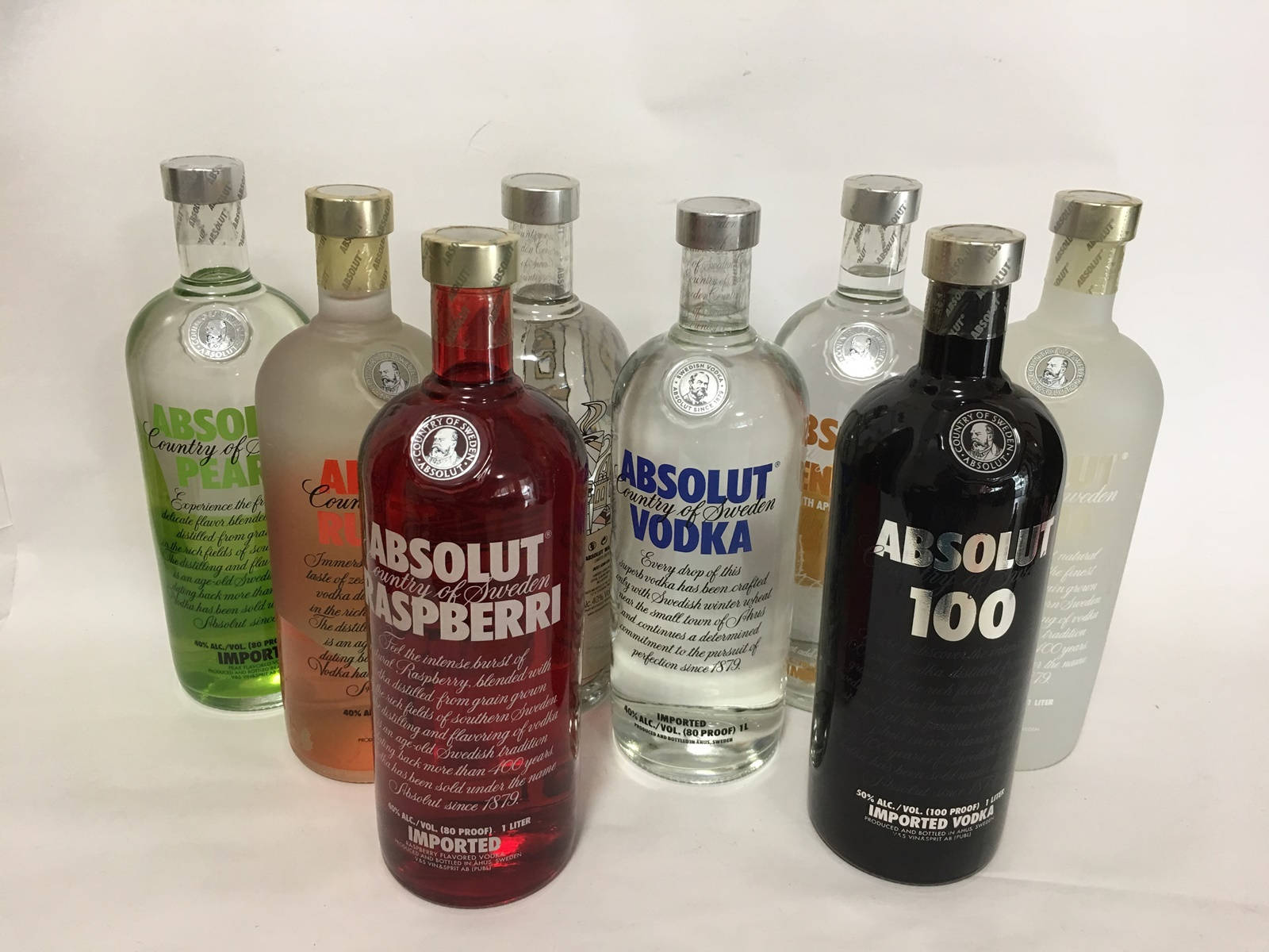 bottle 桌布 壁紙 — 一排色彩繽紛的Absolut伏特加酒瓶，多種口味整齊排列在白色表面上。