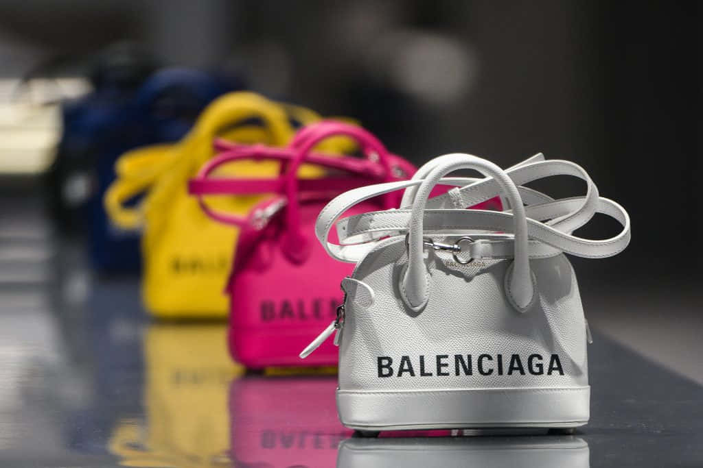 Balenciaga 桌布 壁紙 — 一排色彩繽紛的Balenciaga手袋，有白色、黃色、粉紅色和藍色，排列在反光表面上，景深較淺。