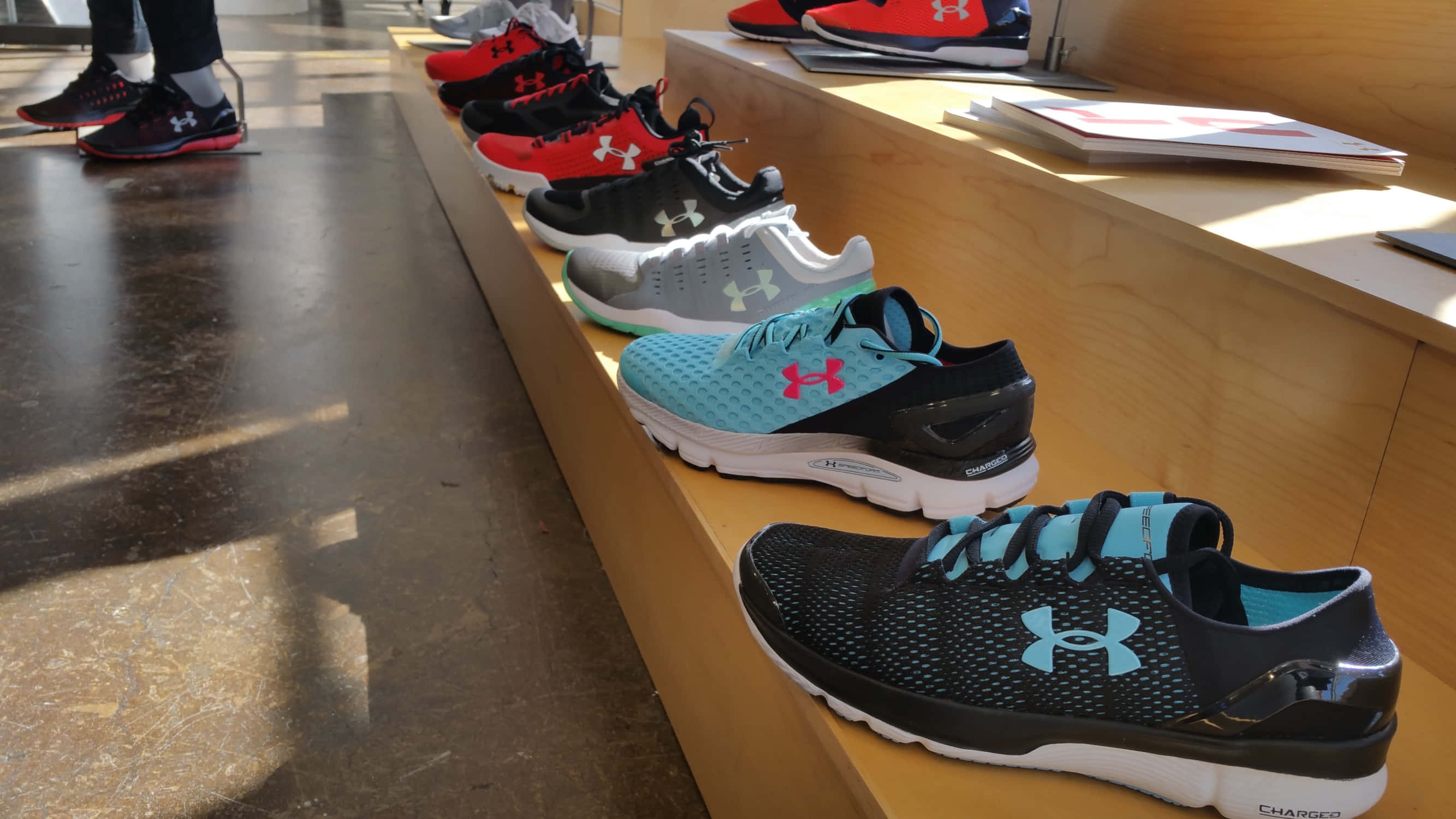 Under Armour 桌布 壁紙 — 一排色彩繽紛的Under Armour跑鞋陳列在光線充足的零售店的木架上。