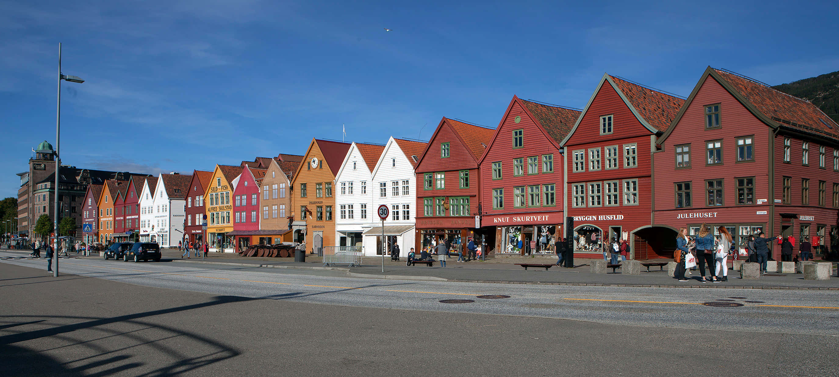 Bryggen 桌布 壁紙 — 一排色彩繽紛的傳統挪威木屋，配以紅色瓦頂，在清澈的藍天下顯得生氣勃勃。