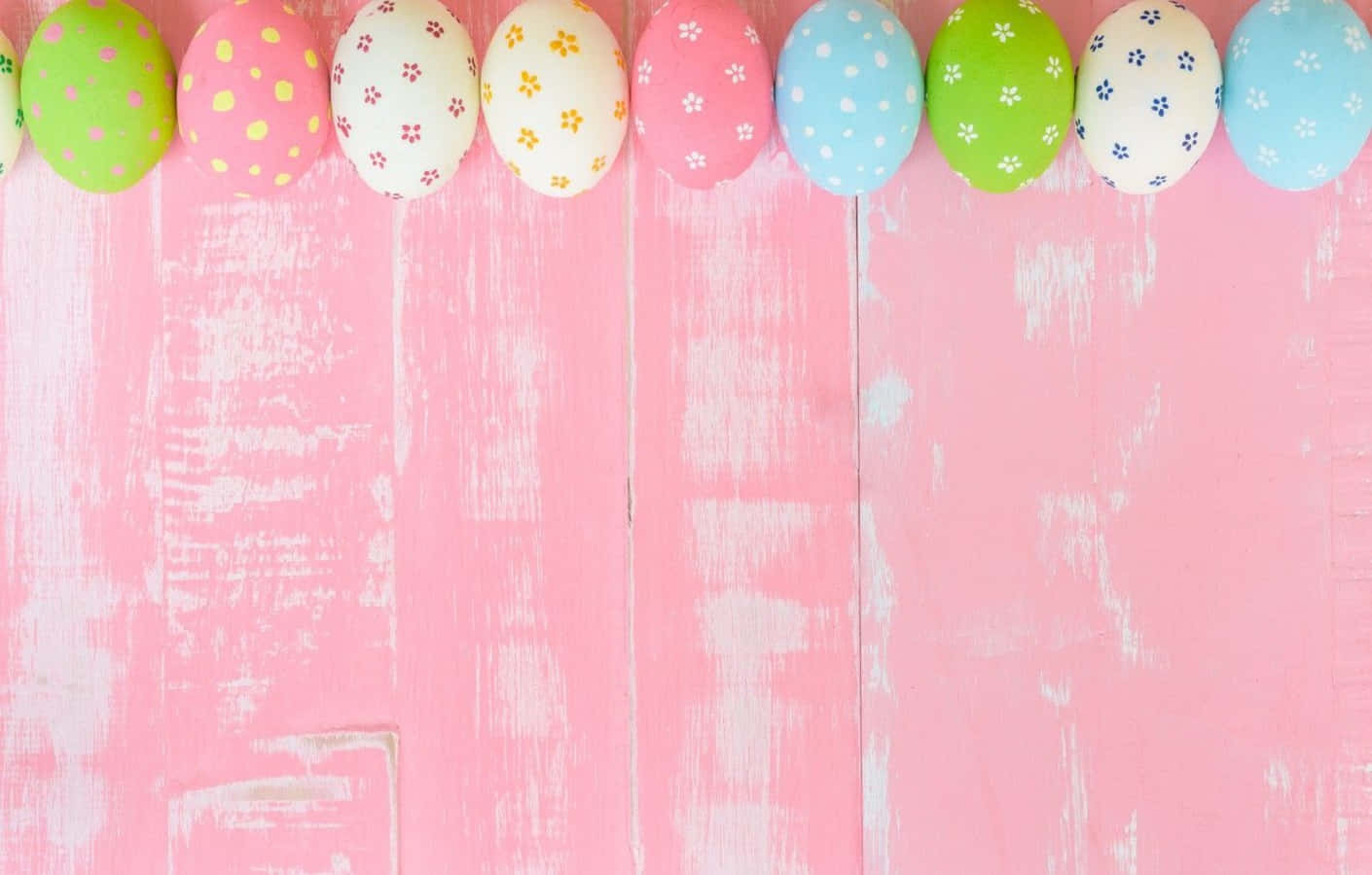 Pastel Easter 桌布 壁紙 — 一排色彩繽紛的圖案復活蛋放在柔軟的粉紅色風化木質表面上。