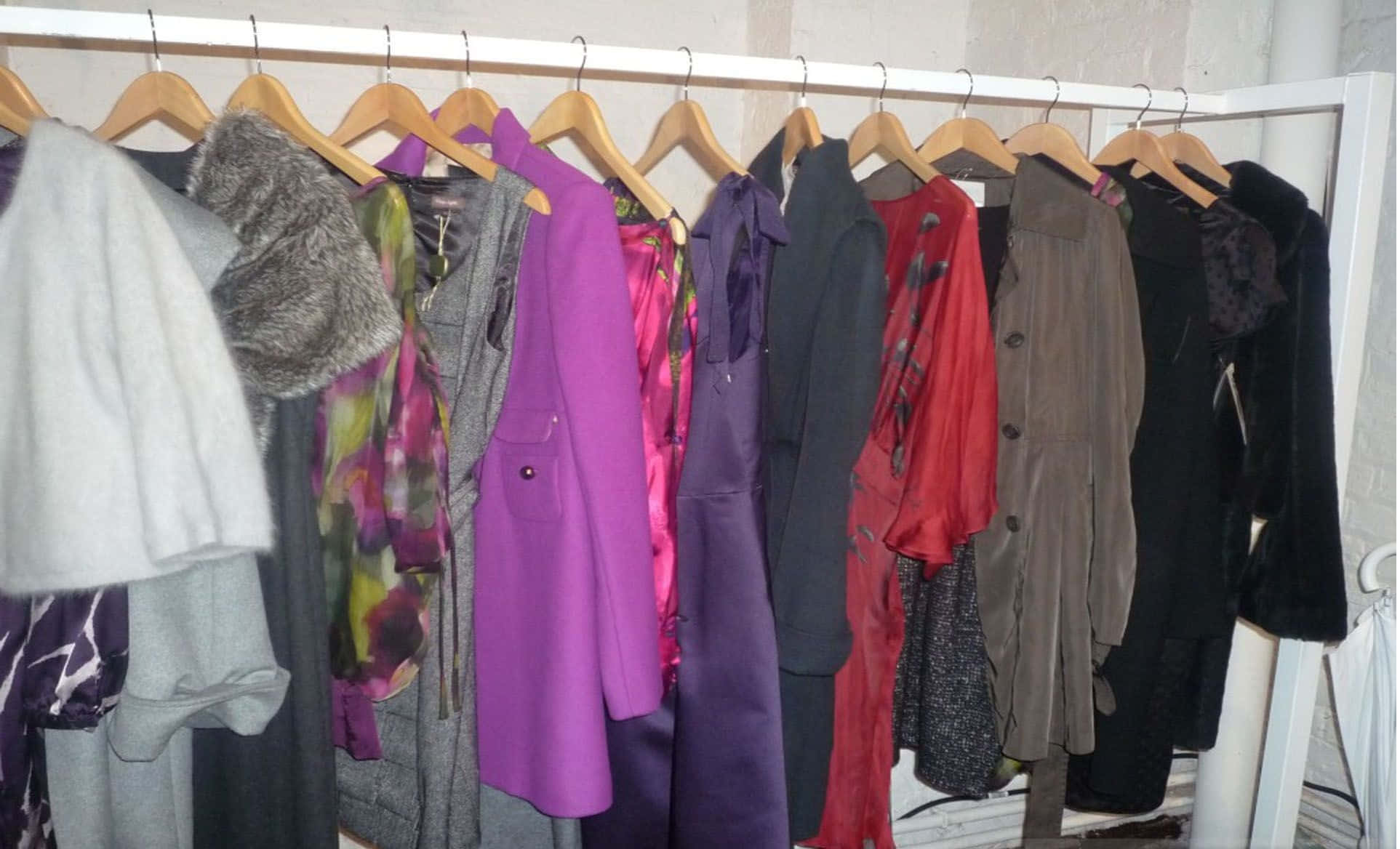 Winter Fashion 桌布 壁紙 — 一排色彩繽紛的外套和夾克整整齊齊地掛在木衣架上，靠著白色牆壁在衣櫃裡。