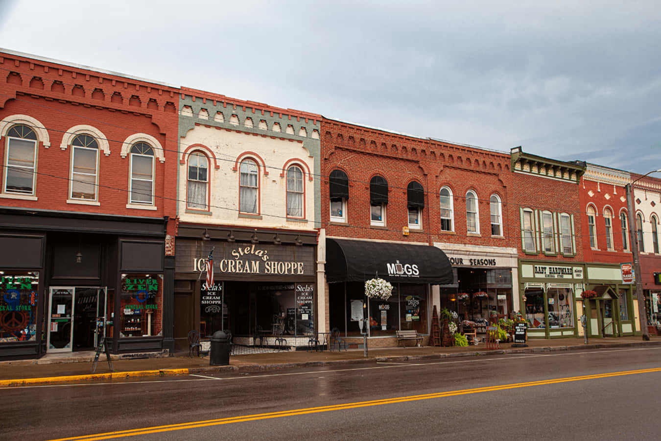 Ashland County 桌布 壁紙 — 一排色彩繽紛的磚砌商店沿著濕漉漉的街道排列，天空多雲，配有復古遮陽篷和商店招牌。