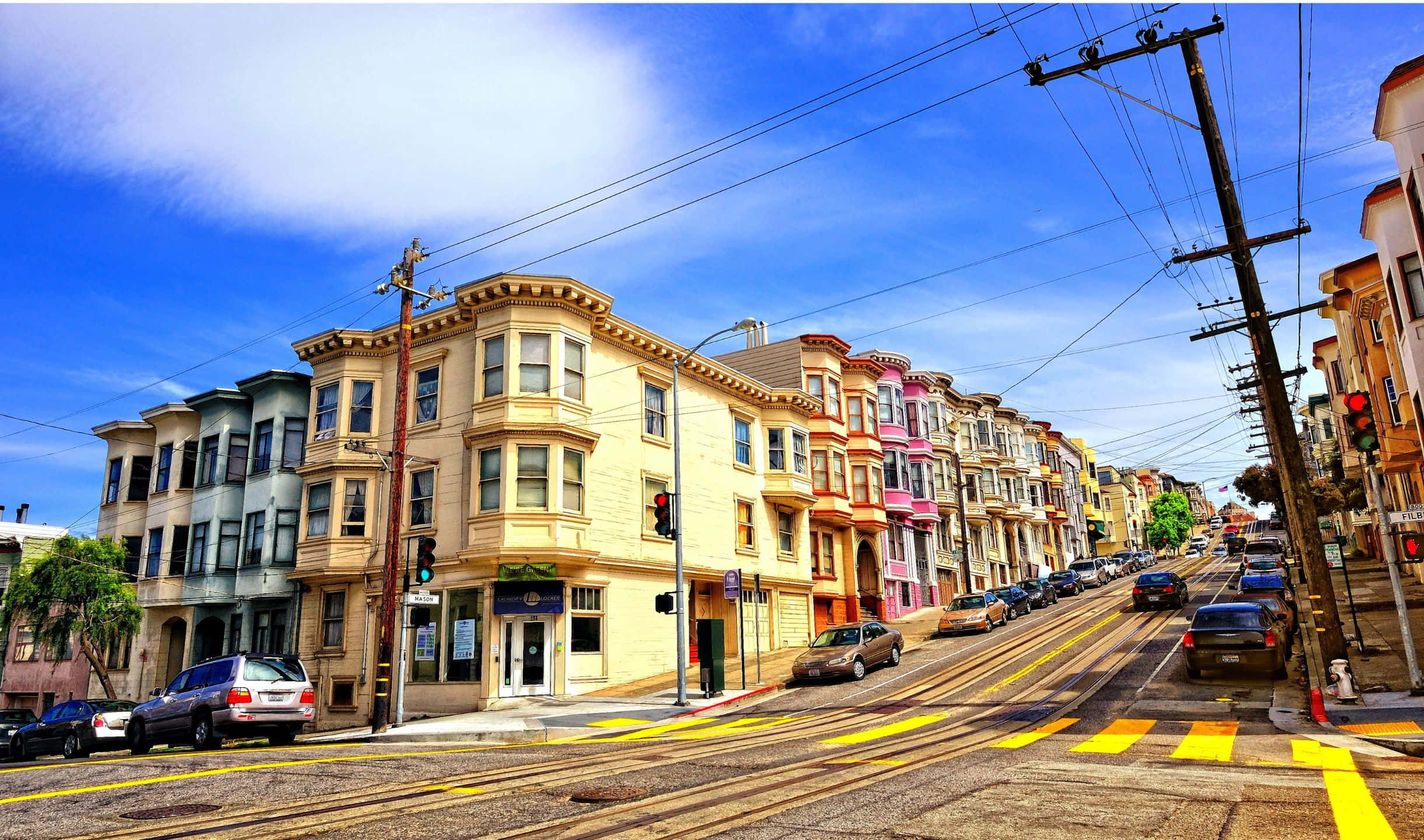 2440x1440 San Francisco 桌布 壁紙 — 一排色彩繽紛的維多利亞式房屋沿著舊金山陡峭的街道排列，上方是明亮的藍天和零星的白雲。