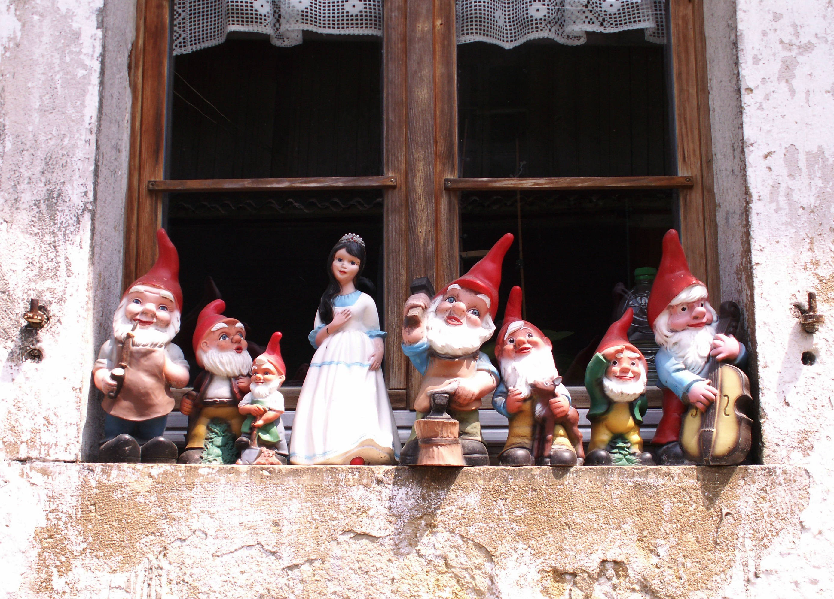 Seven Dwarfs 桌布 壁紙 — 一排色彩繽紛的花園小矮人和公主雕像棲息在風化的石窗台上，窗台下有蕾絲窗簾。